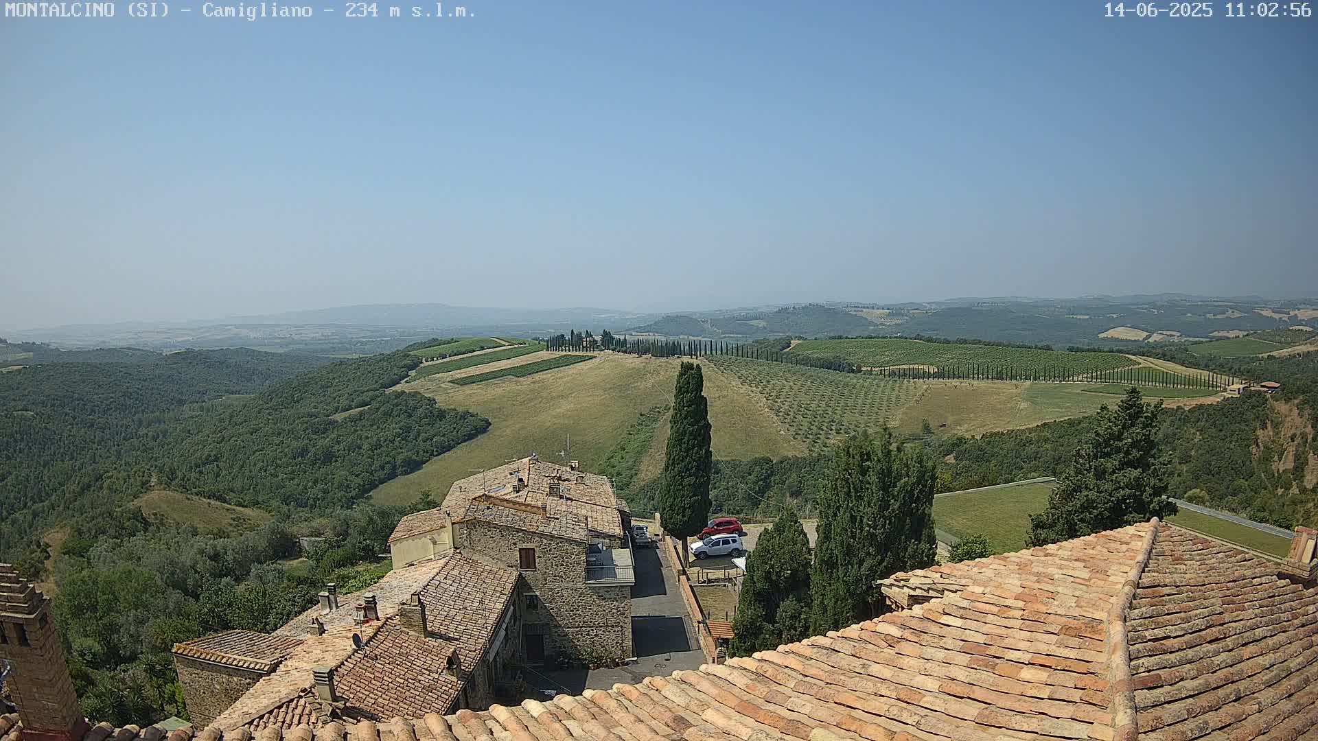 A sun-drenched vista of rolling hills dotted with vineyards and olive groves, overlooked by a village with terracotta rooftops.