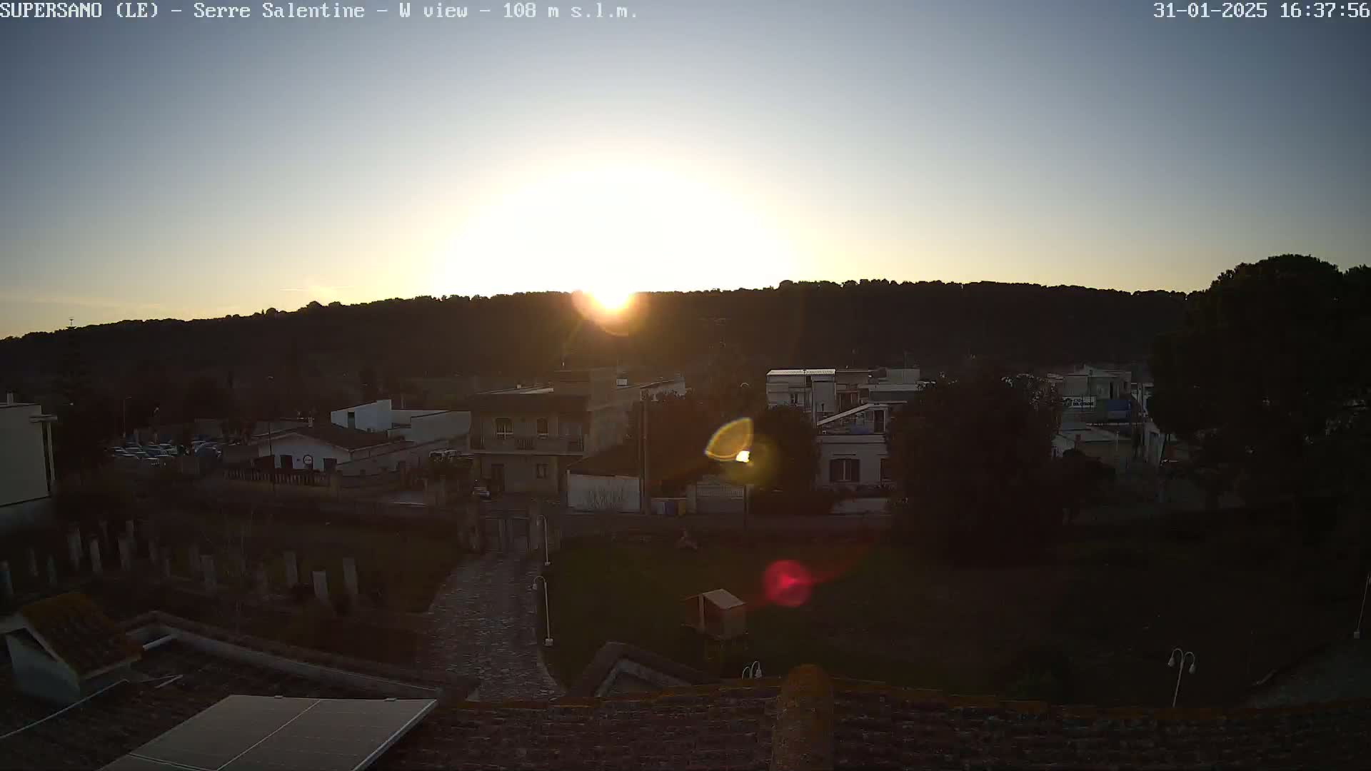 A sunset over a small town nestled against a hillside, with clear skies.