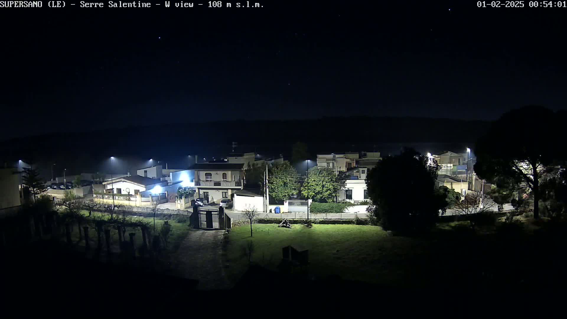 A nighttime, high-angle view of a residential area with houses illuminated by streetlights under a clear, starry sky.