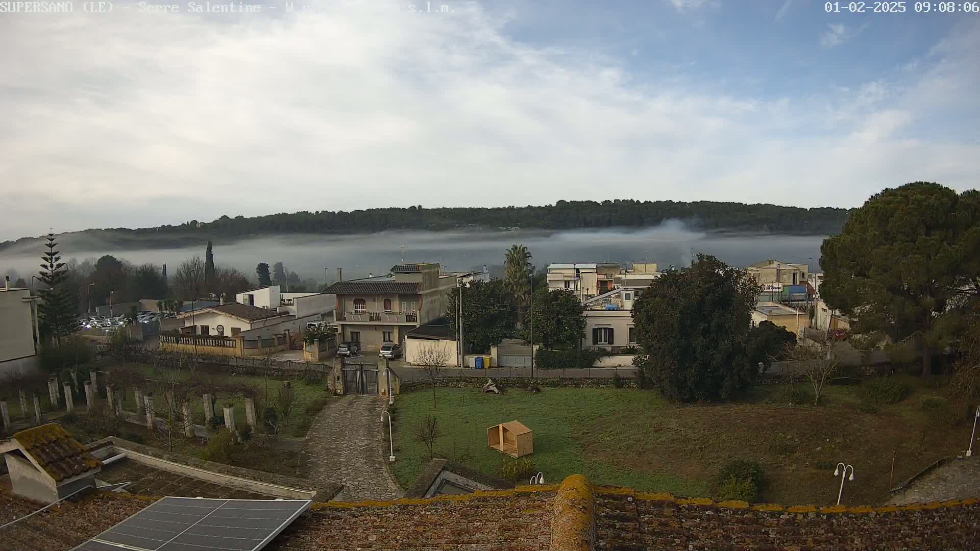 A foggy landscape shows a residential area with houses and trees, viewed from a rooftop with a solar panel.