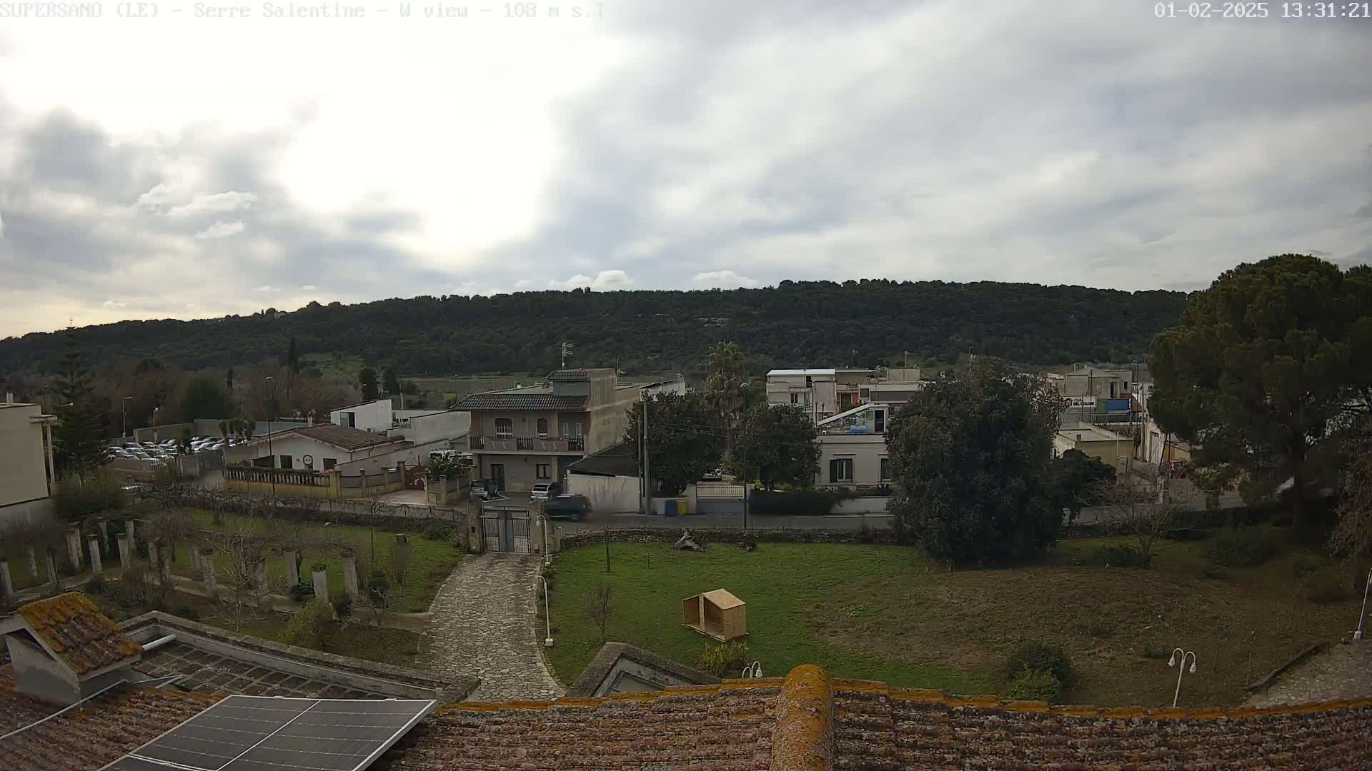 A view from a rooftop shows a residential area with houses, trees, and a paved path under an overcast sky.