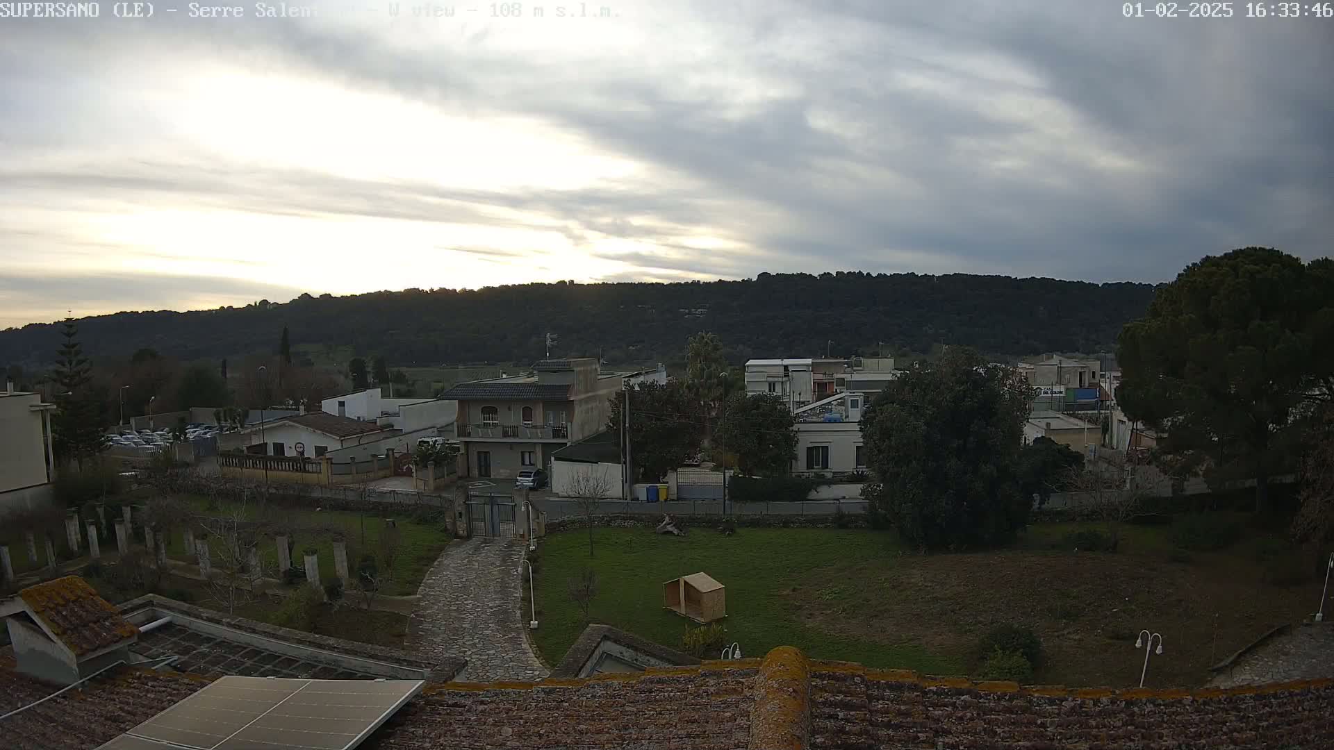 A view from a rooftop shows a residential area with overcast skies and a hill in the background.