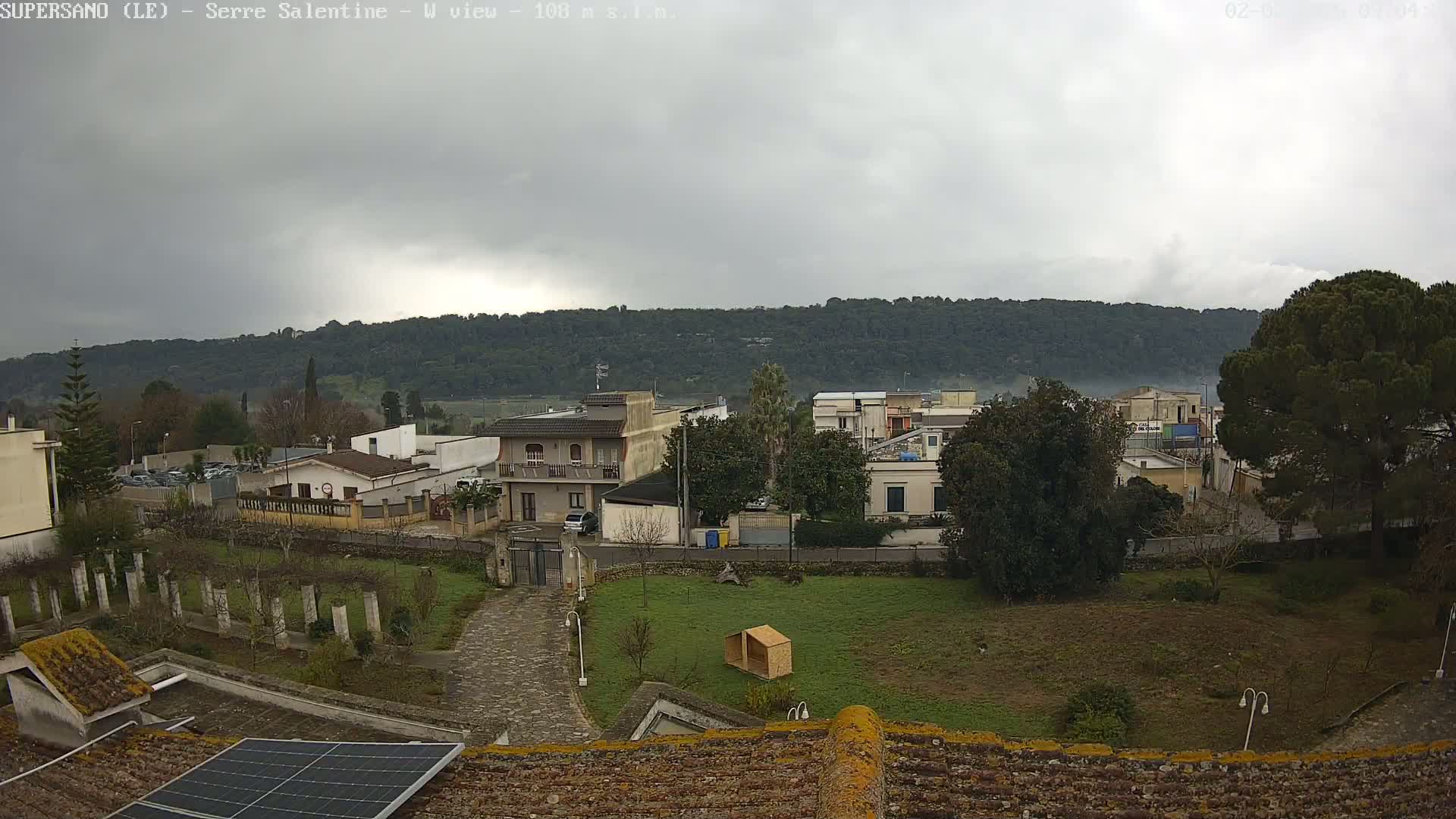 A view of a town nestled against a tree-covered hillside under an overcast sky.