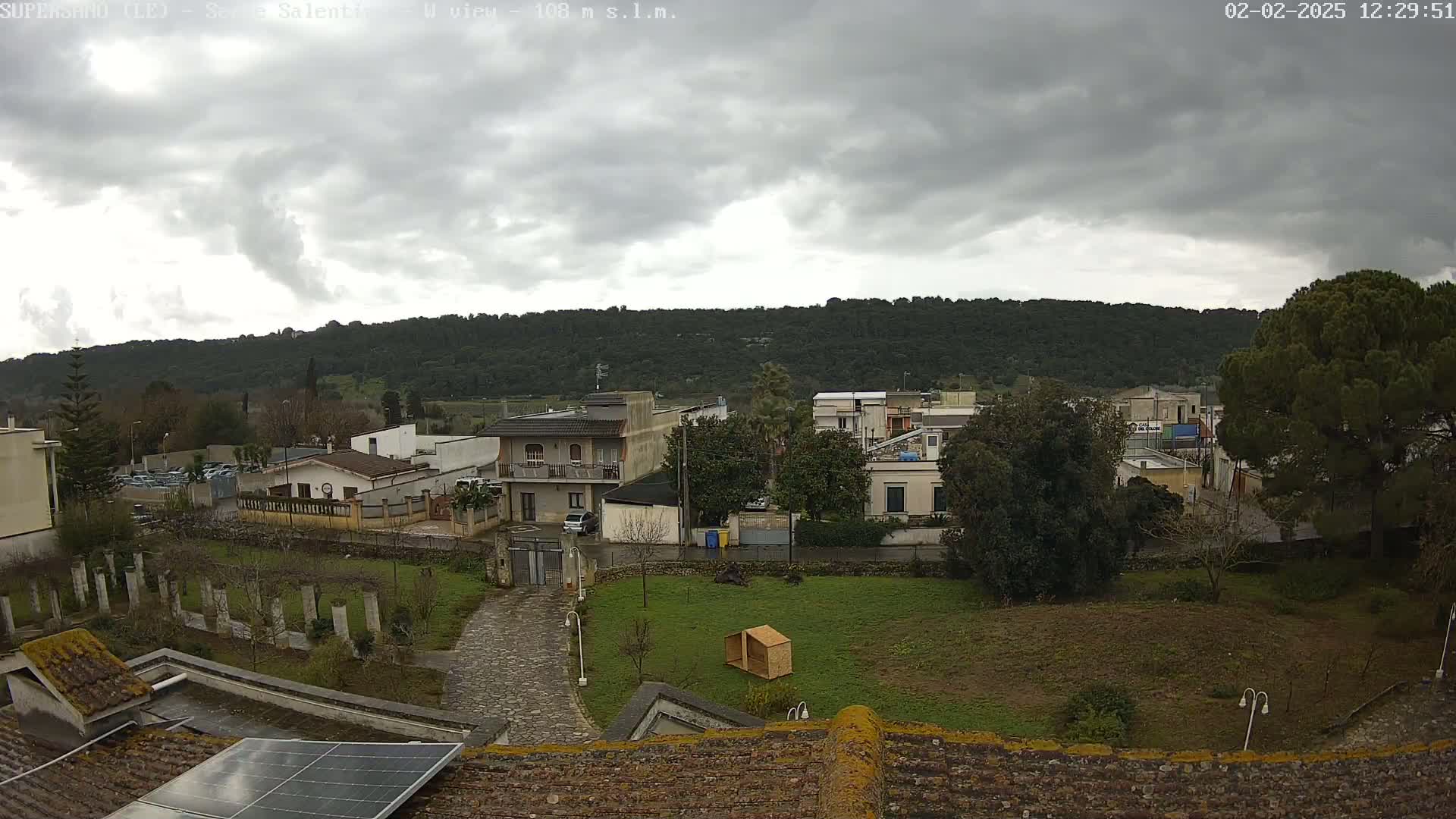 A view of a residential area nestled beside a tree-covered hill under an overcast sky.