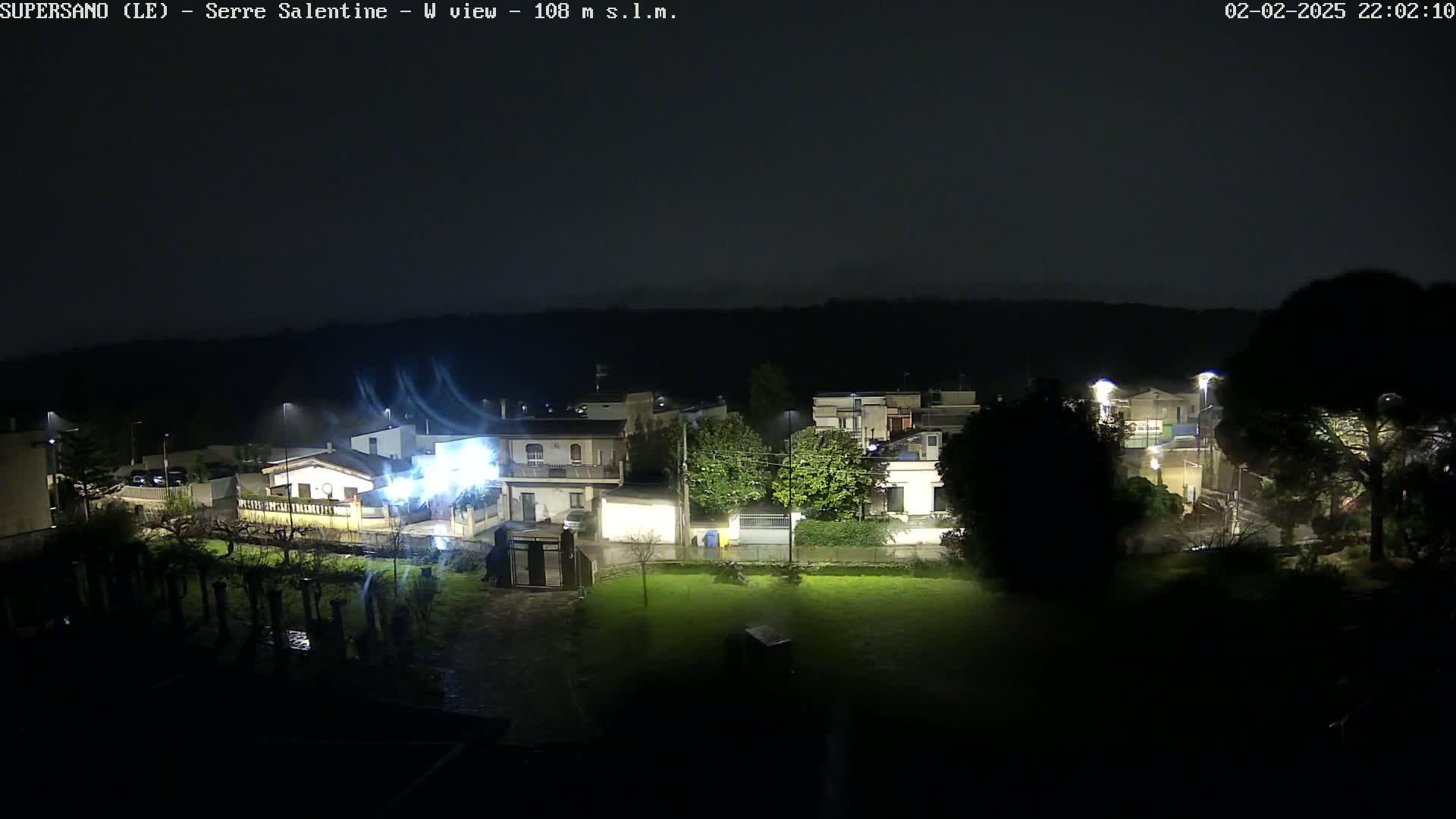 A nighttime view of a residential area illuminated by streetlights during a rainy, windy storm.