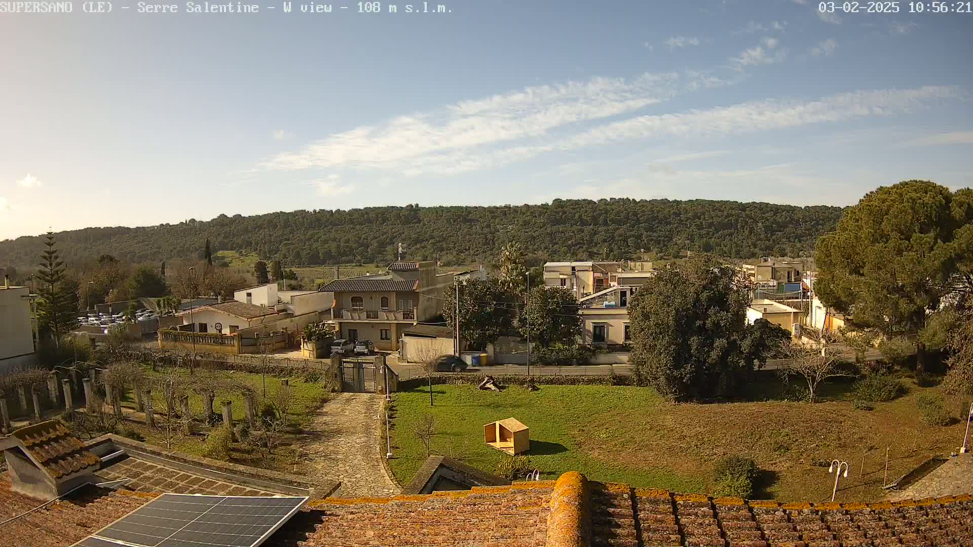 A mostly sunny day overlooks a residential area nestled against a tree-covered hillside.