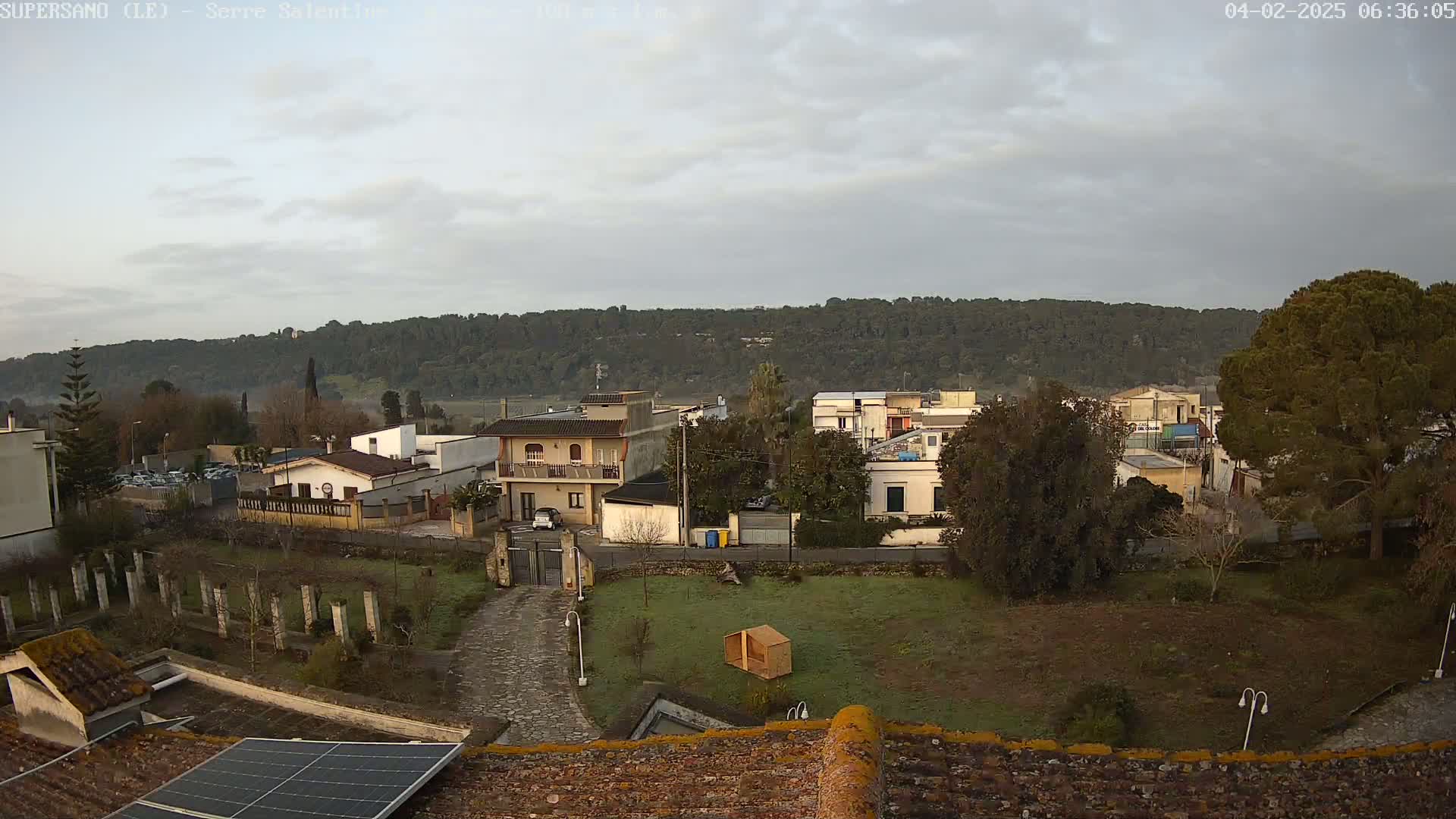 A view from a rooftop shows a small town nestled against a hillside under a mostly cloudy sky.