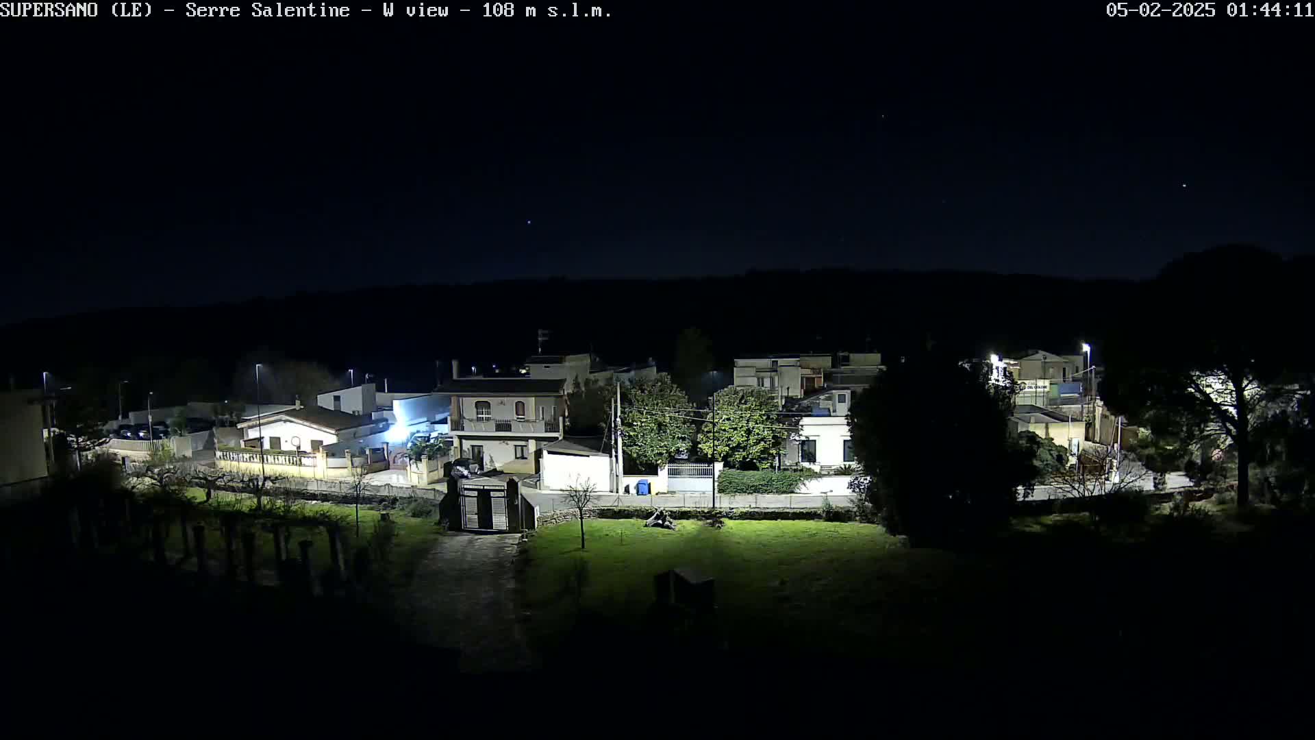 A nighttime view of a residential area with houses illuminated under a clear, dark sky.