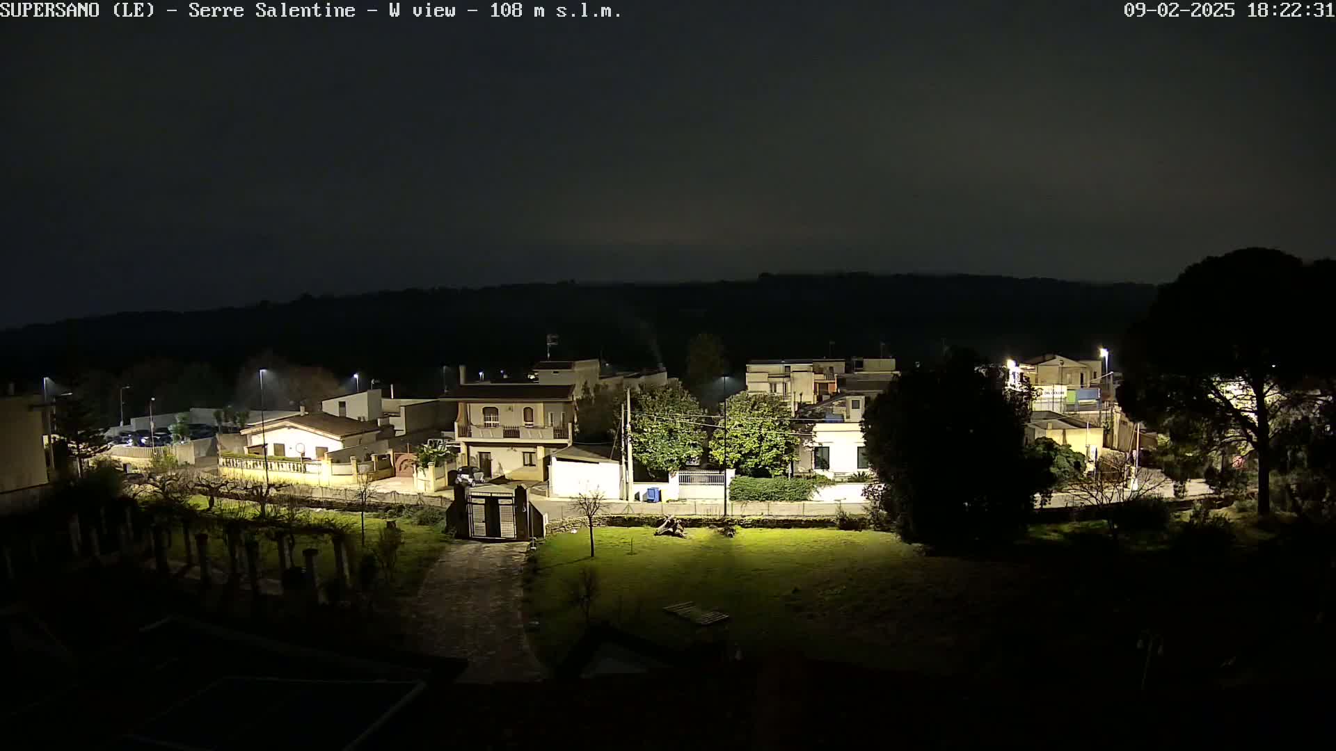 A nighttime view of a residential area with houses and streetlights, under a dark, clear sky.