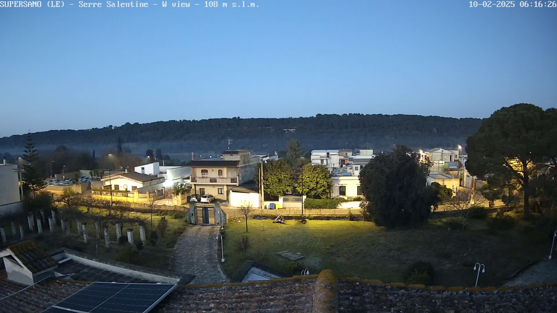 A nighttime view of a small town nestled against a hill under a clear, twilight sky.