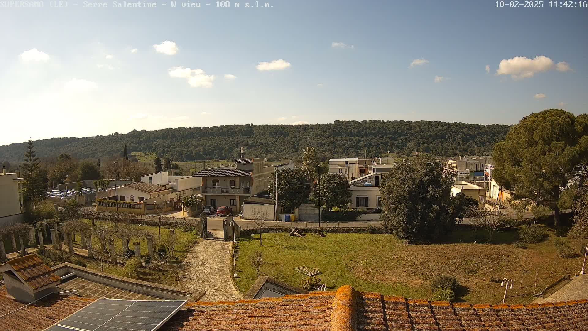 A partly cloudy day reveals a view of a residential area nestled beside a tree-covered hillside.