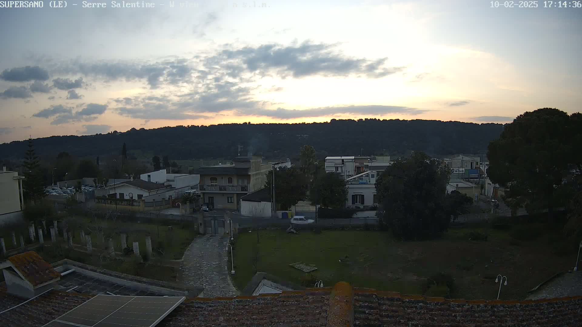 A partly cloudy sunset over a residential area with hills in the background.