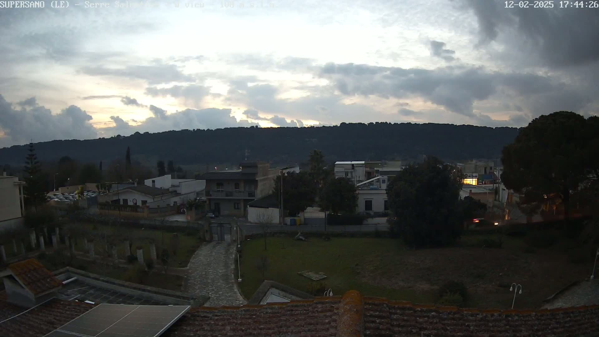A cloudy sunset over a small town nestled against a dark, hilly landscape.