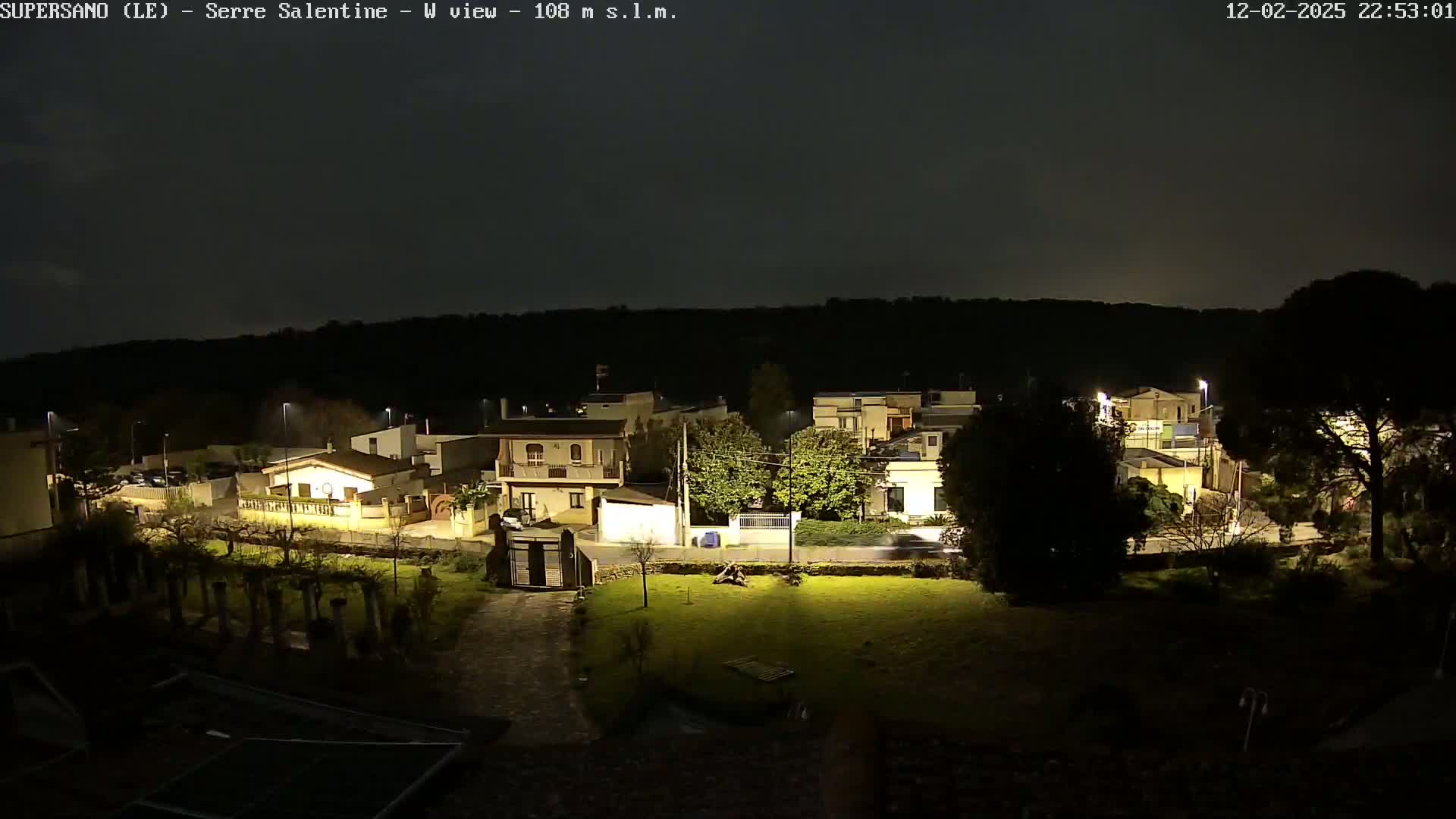 A nighttime view of a residential area with houses illuminated, under a dark, clear sky.