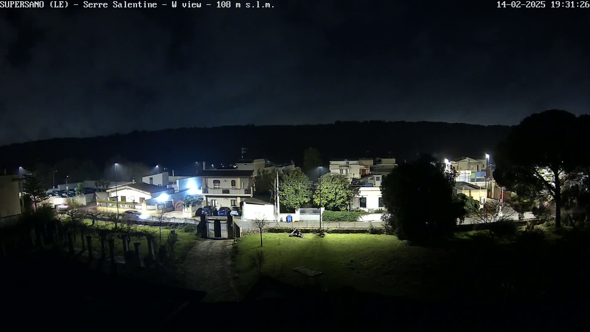 A nighttime view of a residential area illuminated by streetlights, under a dark sky.