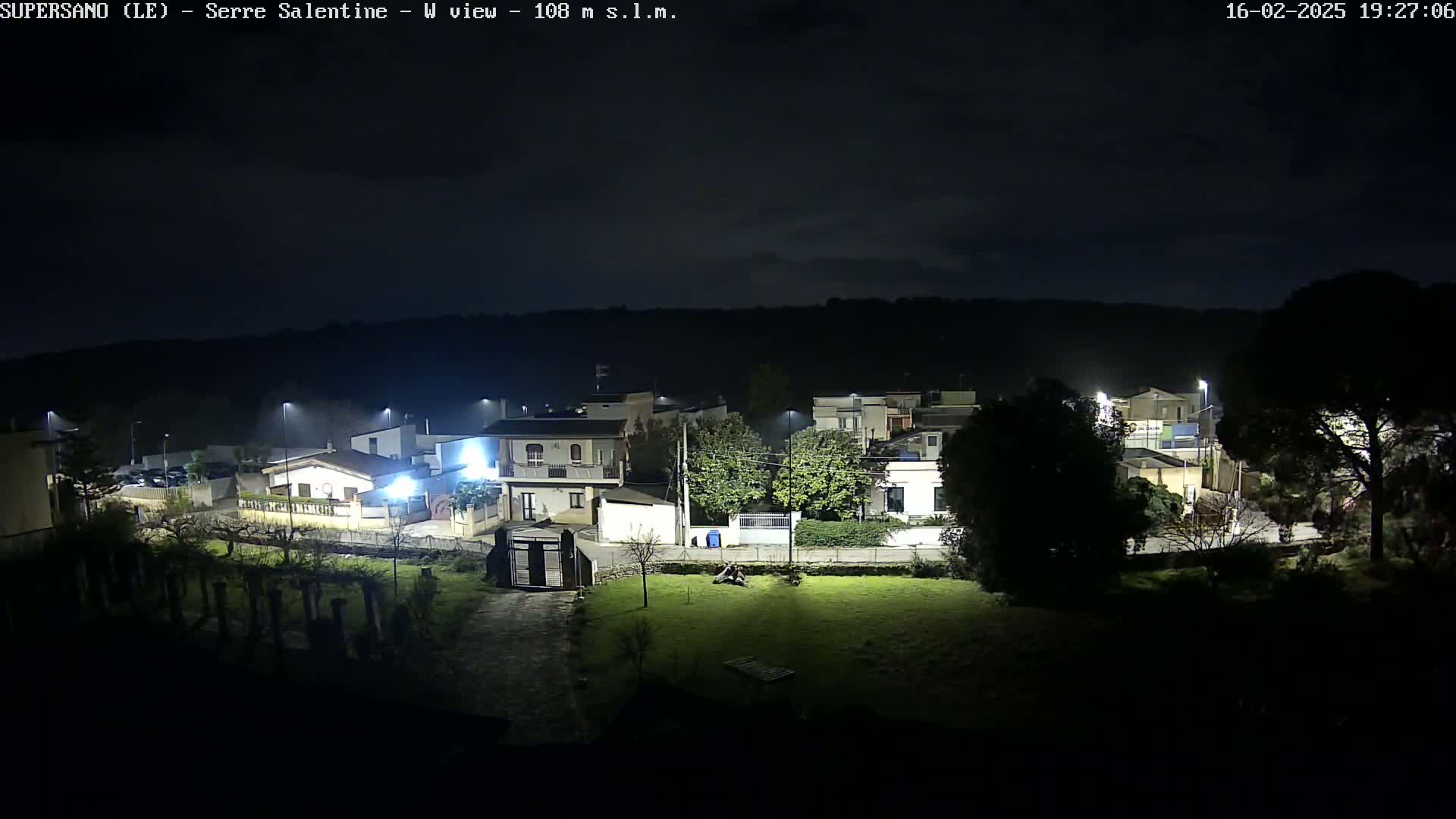 A nighttime view of a residential area illuminated by streetlights under a mostly clear, dark sky.