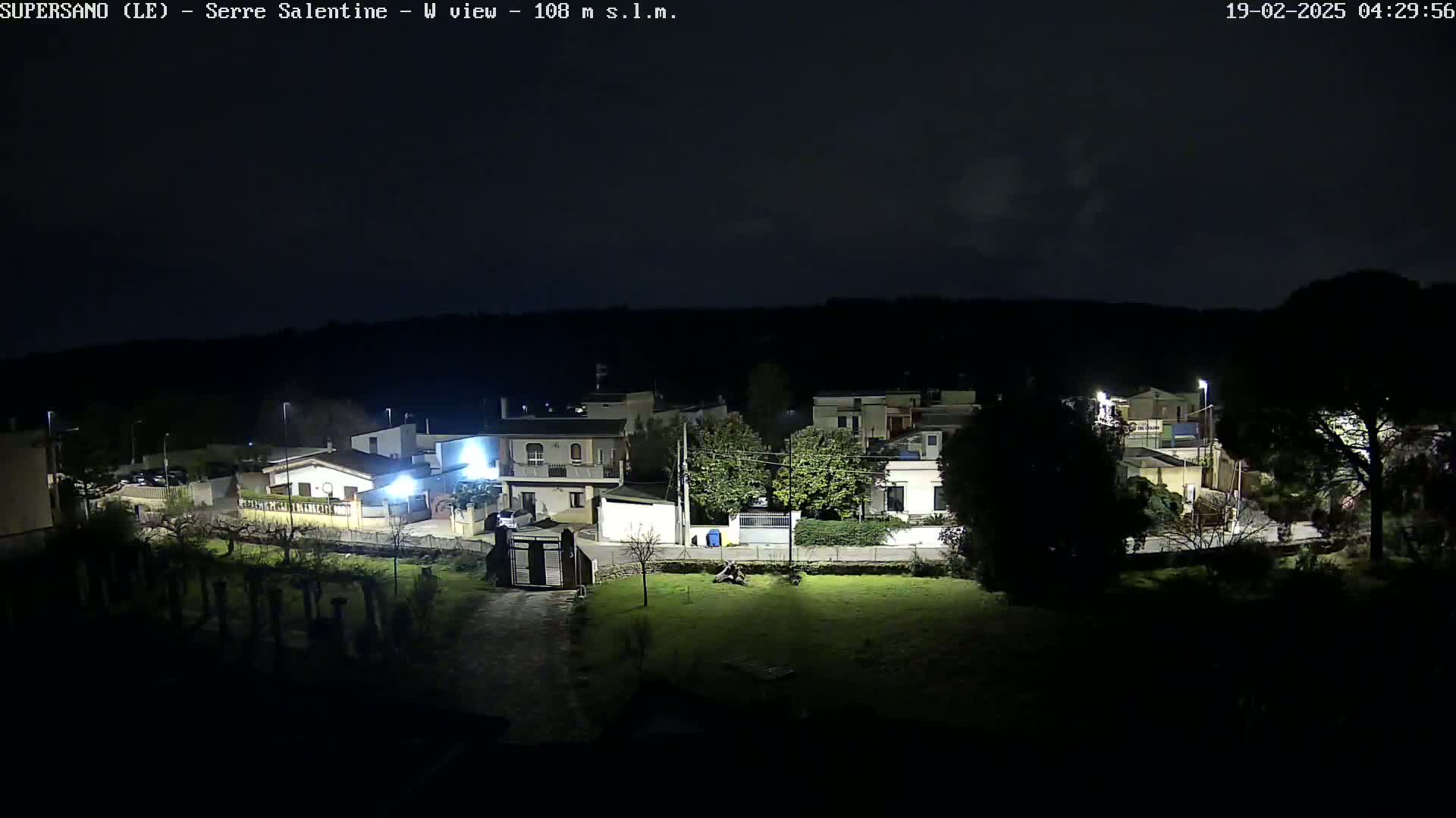 A nighttime view of a residential area with houses and streetlights under a dark sky.