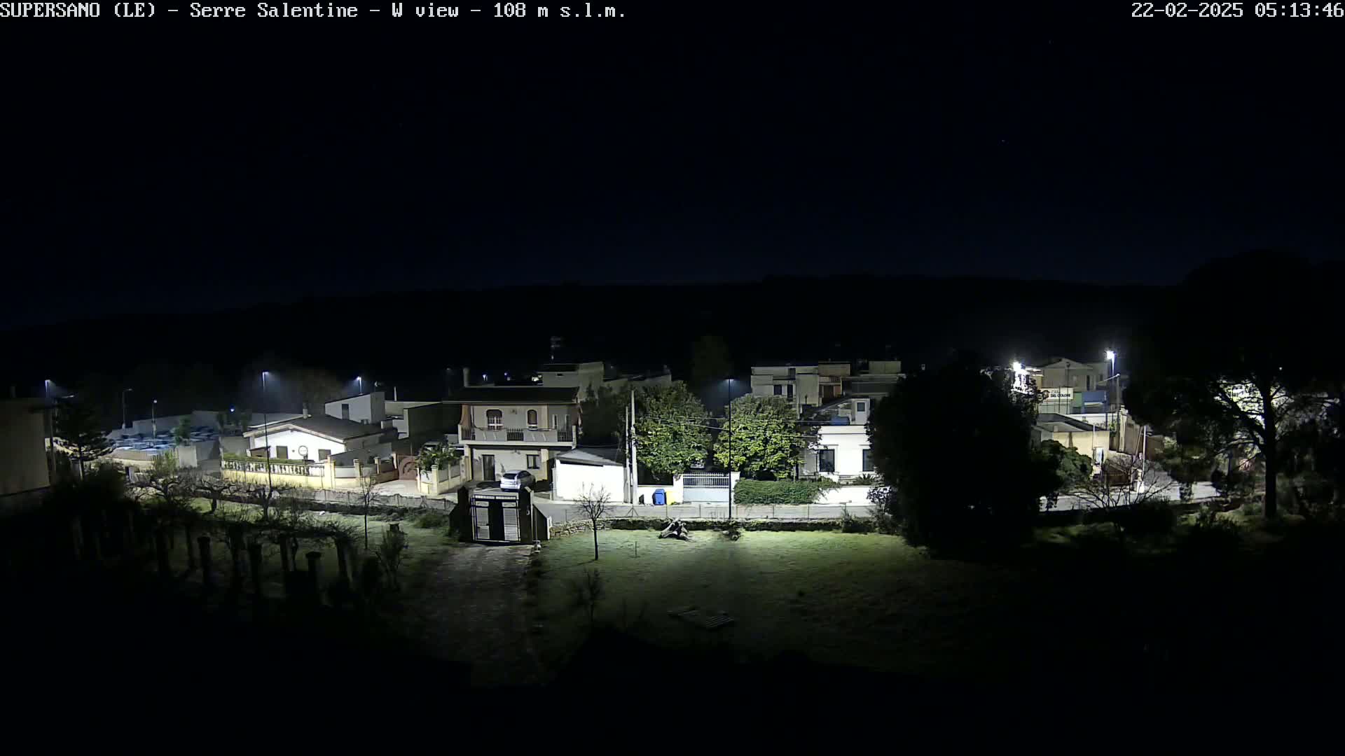 A nighttime, low-angle view of a residential area illuminated by streetlights, with a grassy area in the foreground.
