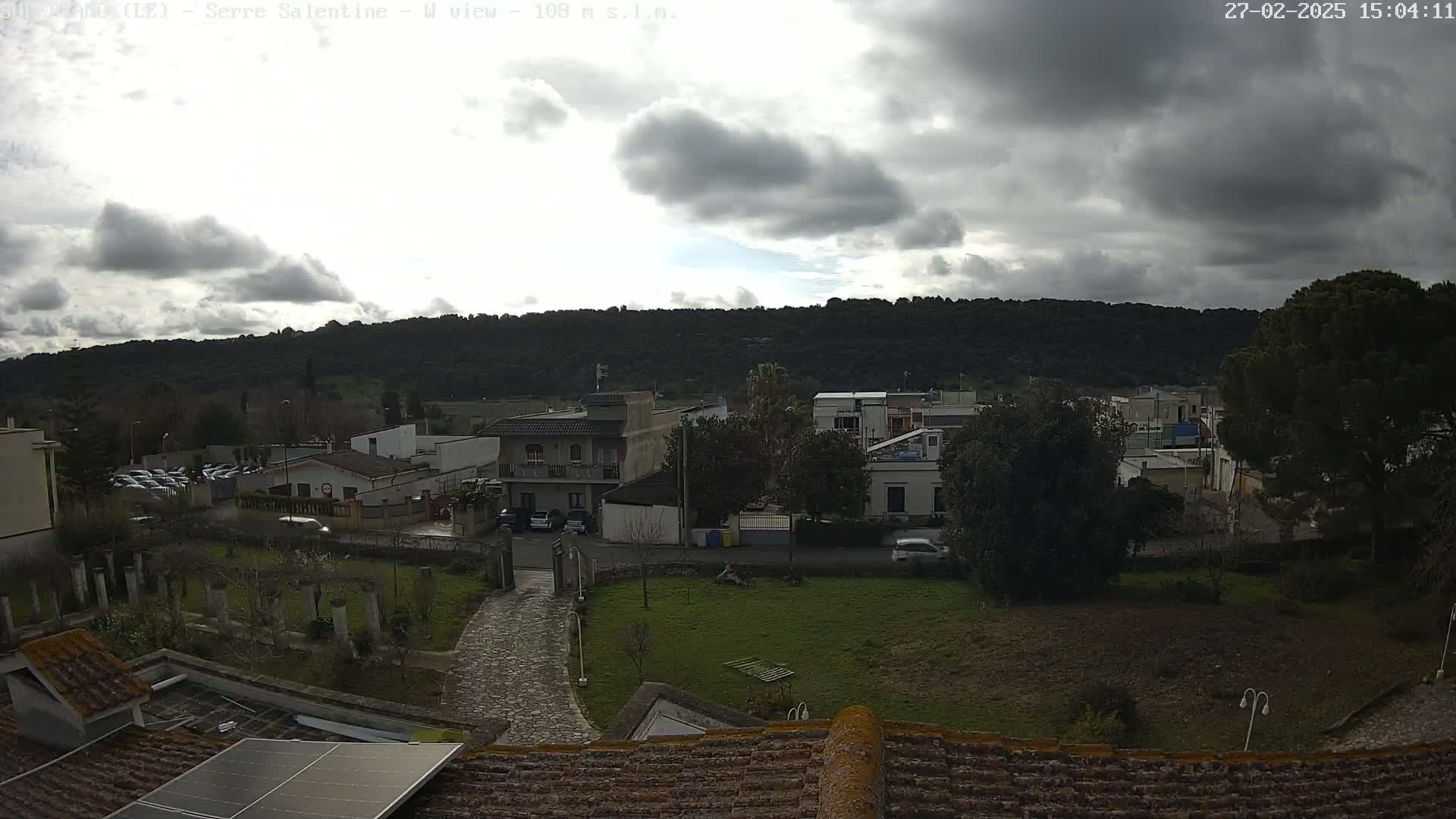 A view from a rooftop shows a residential area with overcast skies and a hill in the background.