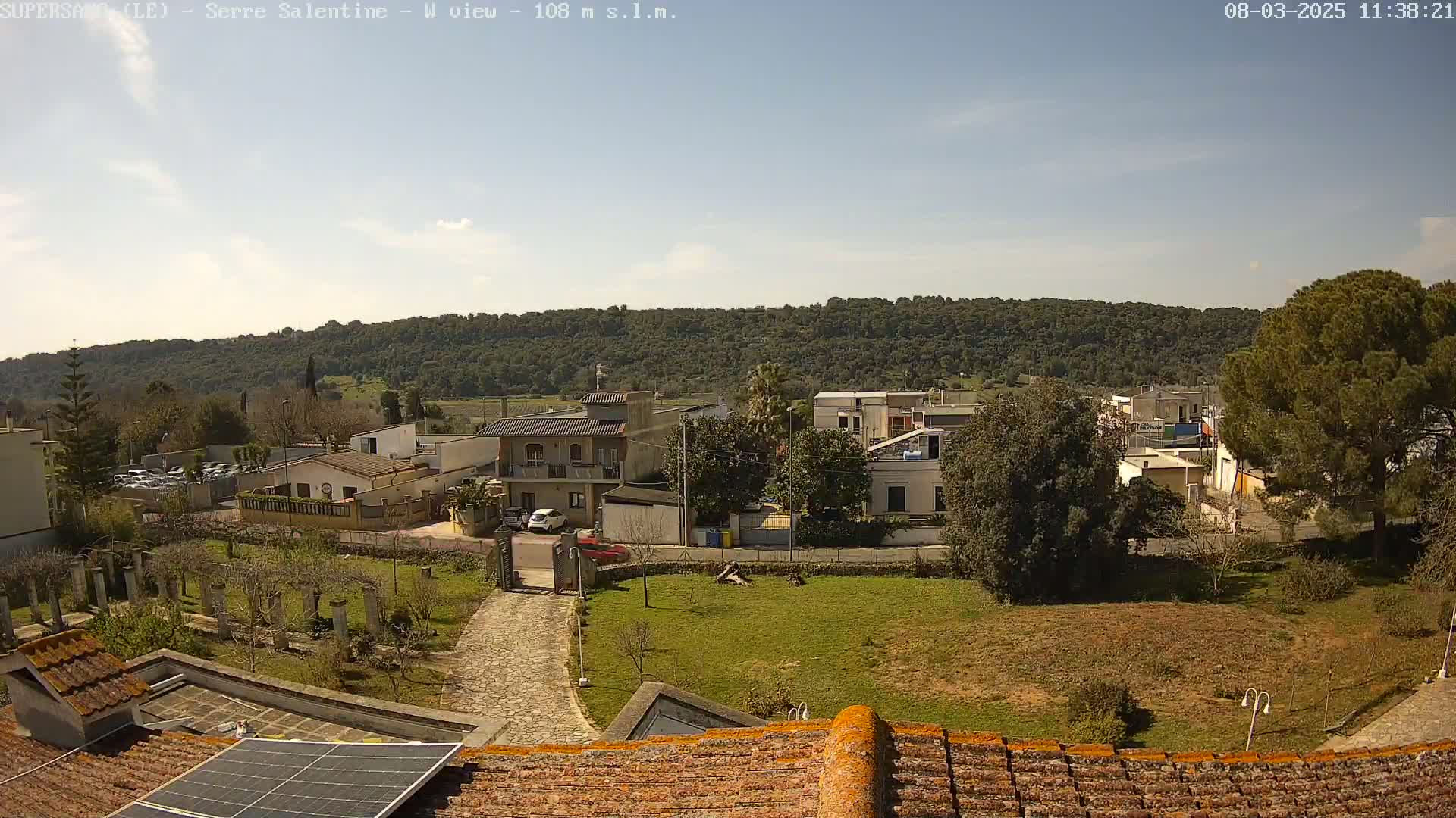 A sunny day reveals a view of a small town nestled against a verdant hillside, seen from a rooftop with a solar panel.