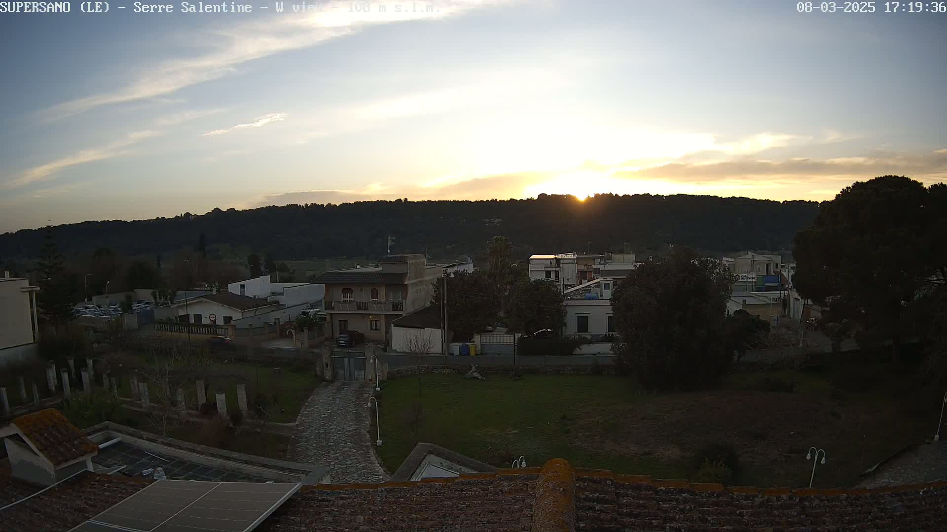 A sunset over a residential area with hills in the background, under a mostly clear sky.
