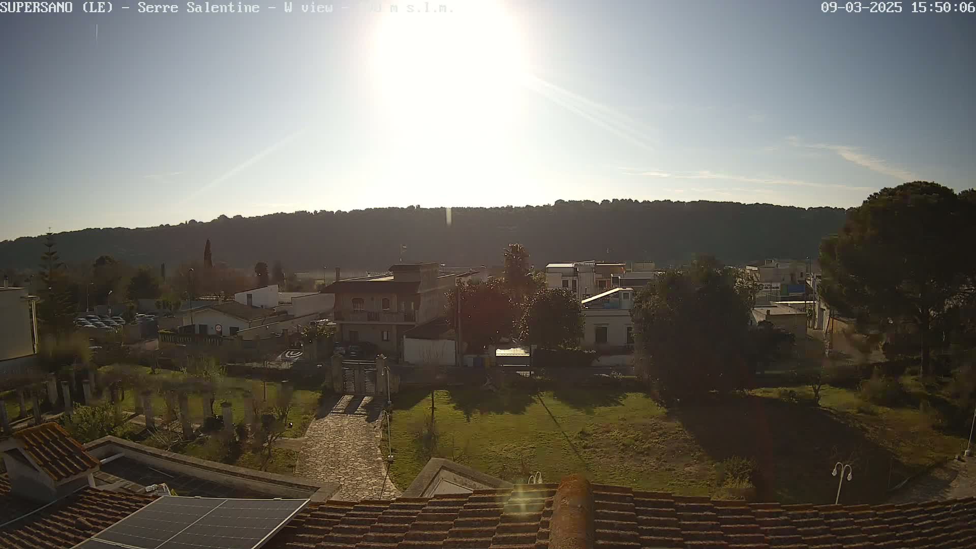 A sunny day reveals a view of a small town nestled against a hillside, seen from a rooftop with a solar panel.