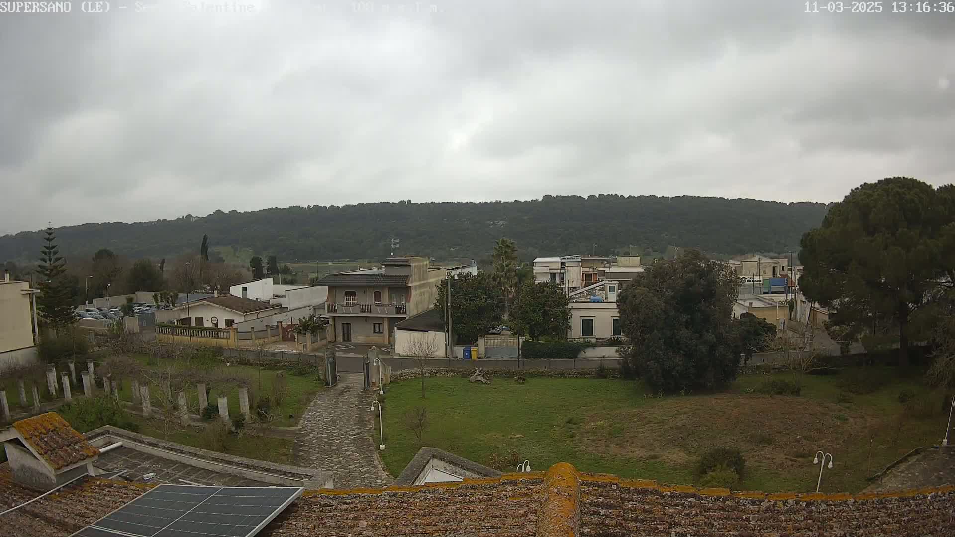 A view from a rooftop shows a small town under an overcast sky, with a hillside in the background.