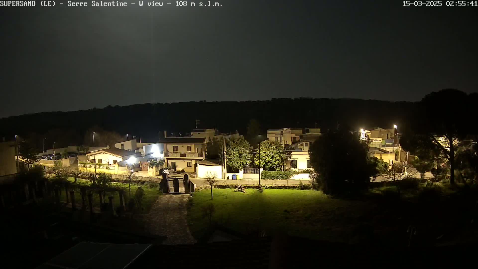 A nighttime view of a residential area with illuminated buildings and streetlights under a dark, clear sky.
