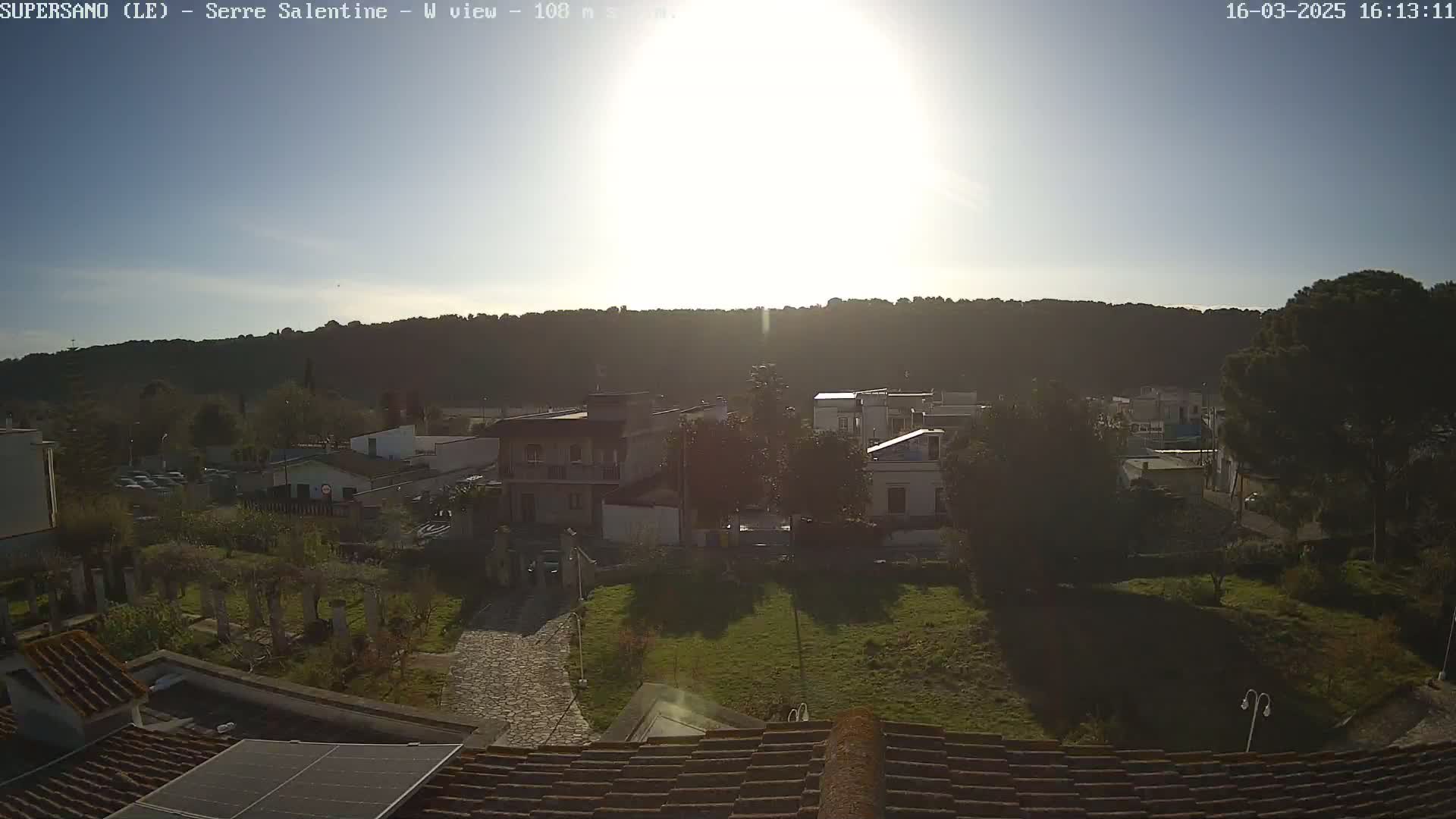 A sunny view of a small town nestled against a hillside, seen from a rooftop with a solar panel.