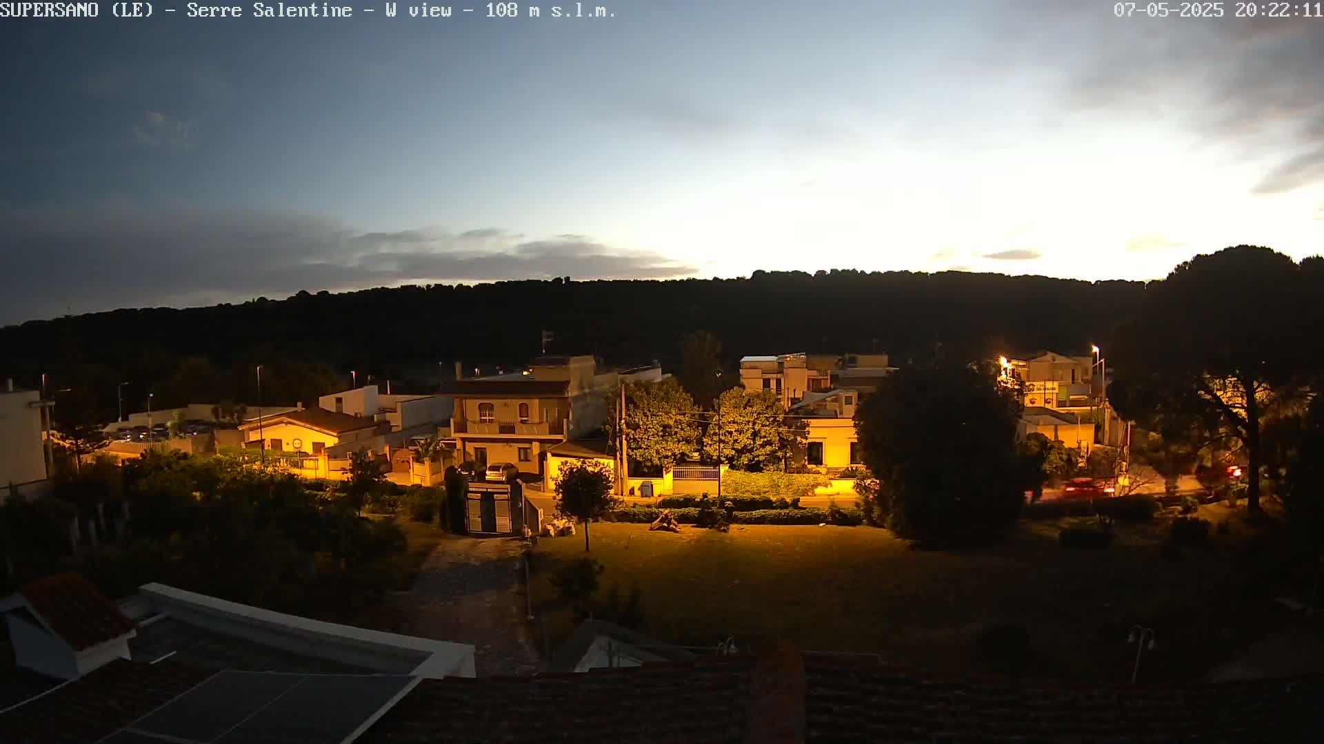 A nighttime view of a residential area nestled against a hill under a twilight sky.