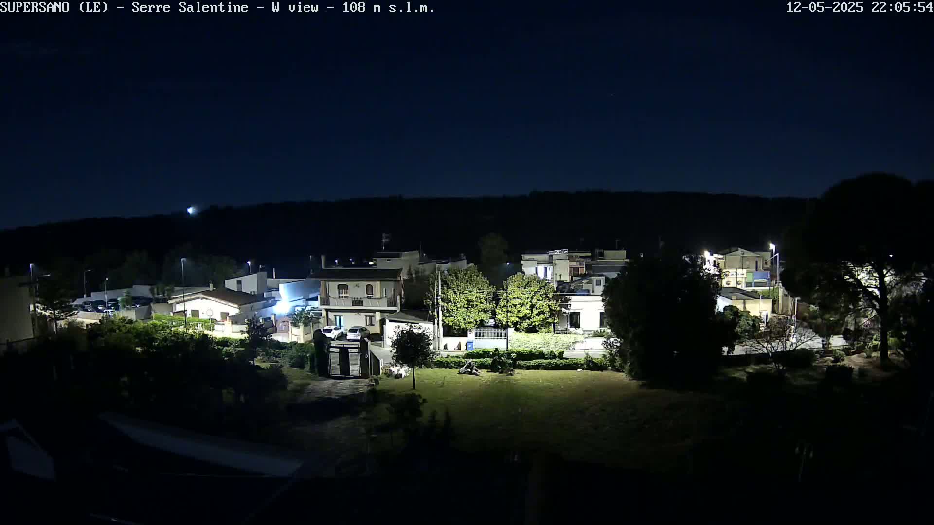 A nighttime view of a residential area with houses and trees under a clear, dark sky.