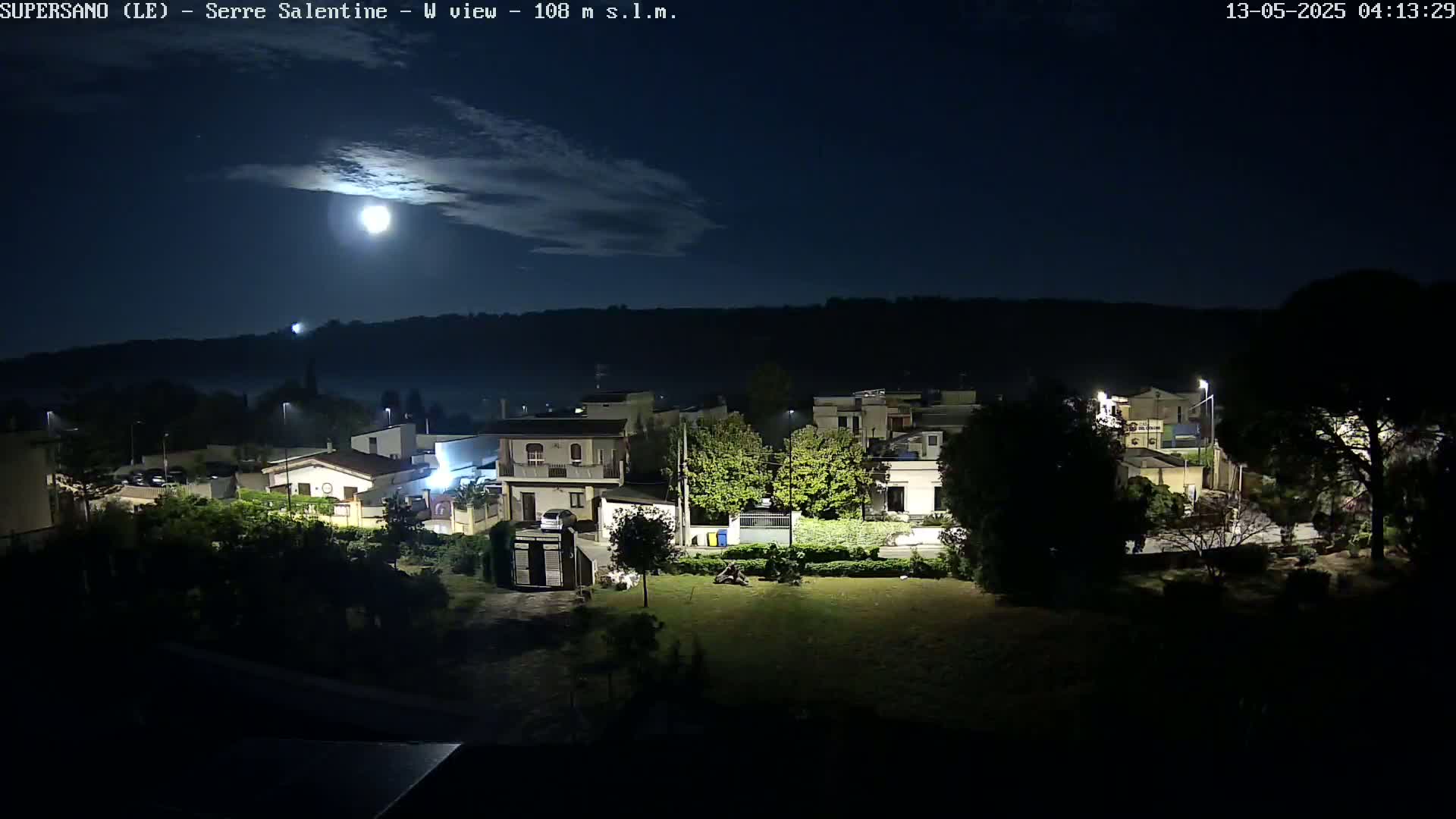 A nighttime view of a residential area under a partly cloudy sky with a bright moon.