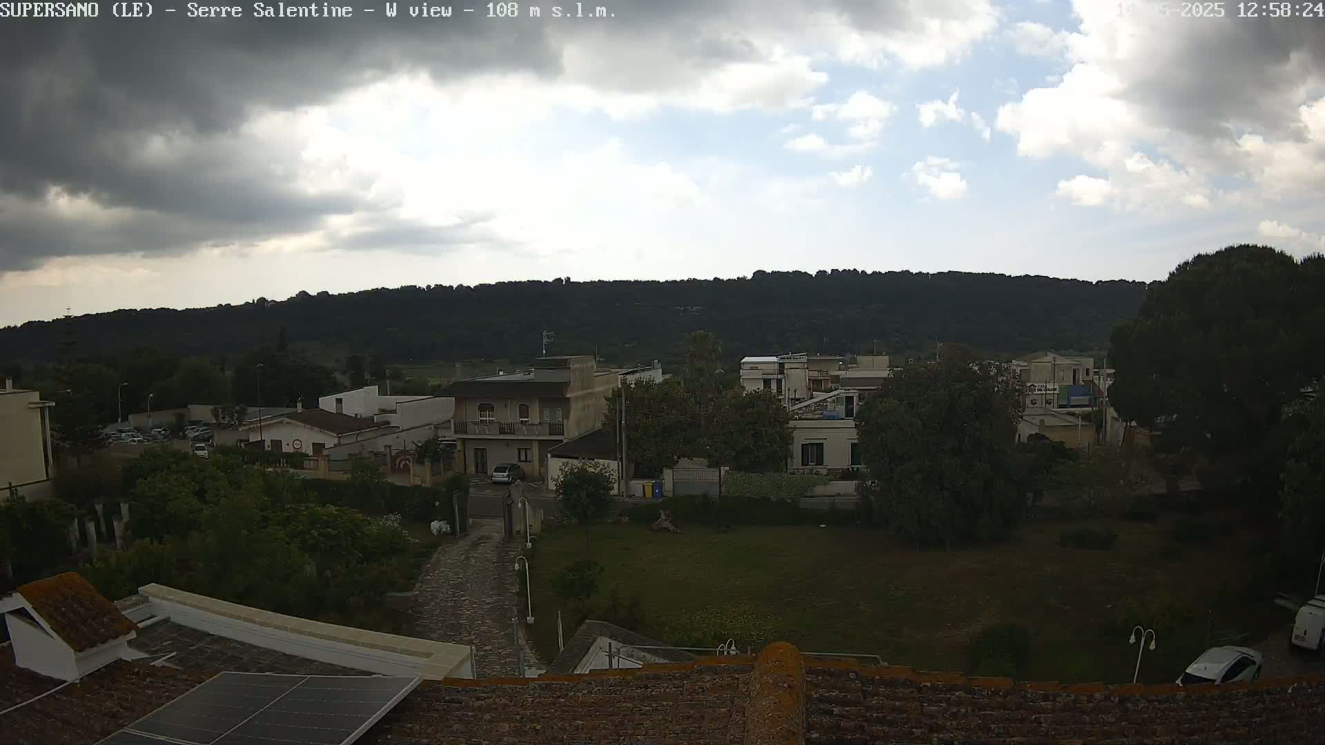 A partly cloudy sky overlooks a residential area nestled against a verdant hillside.