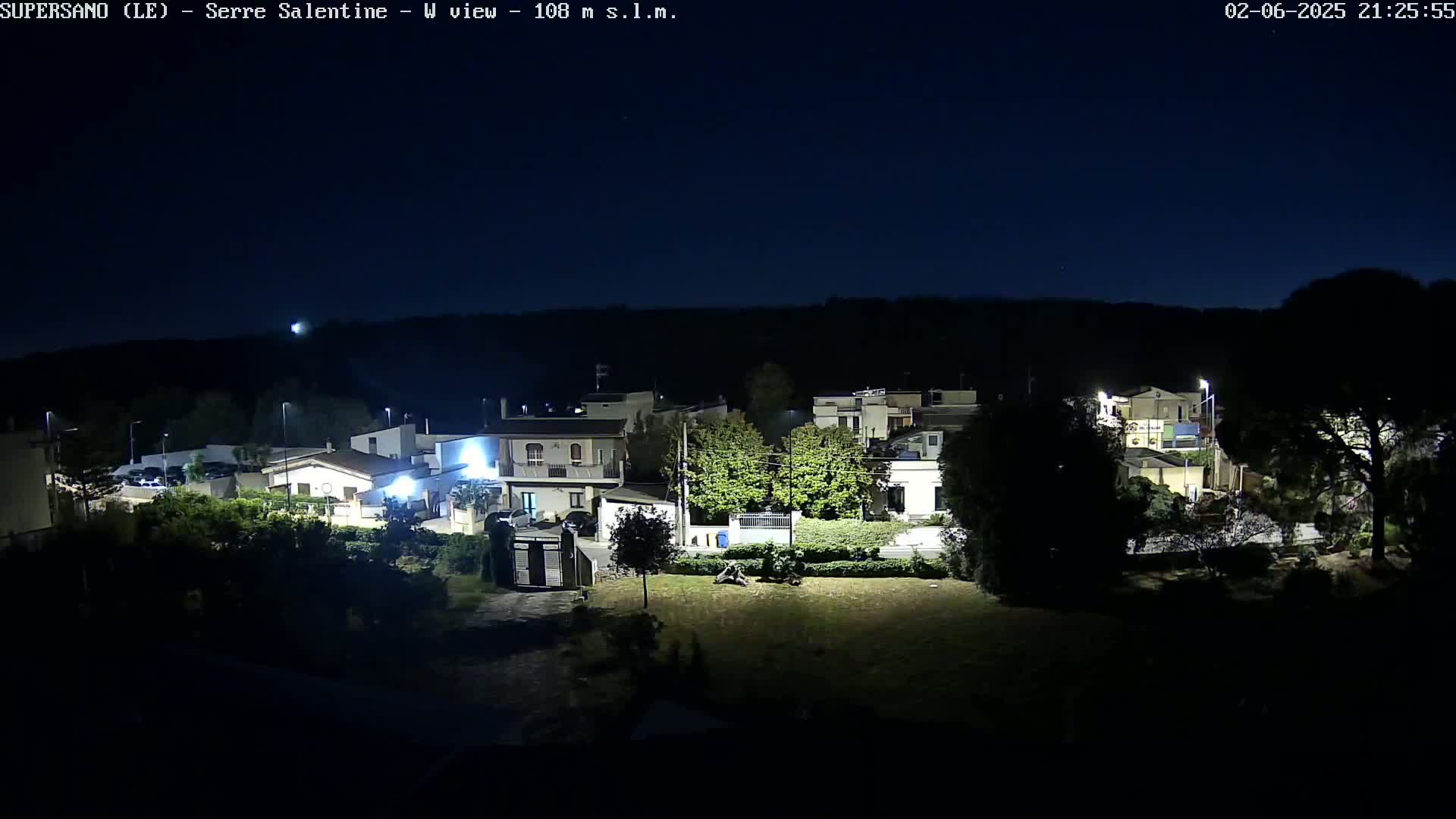 A nighttime view of a residential area with houses and trees under a clear, dark sky.