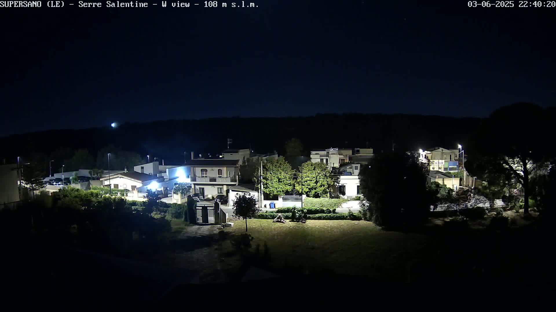 A nighttime view of a residential area with houses and trees under a clear, dark sky.