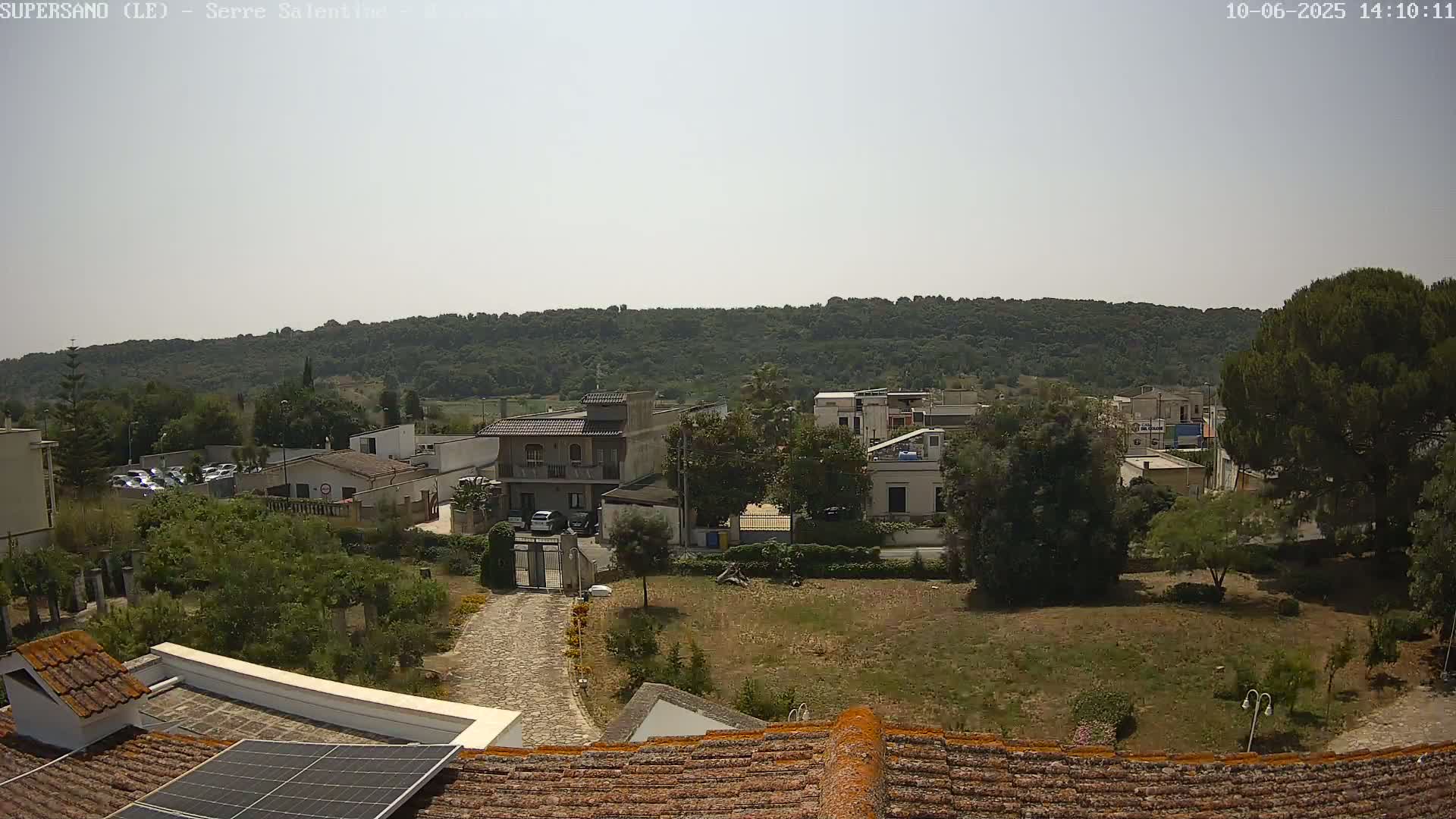 A sunny day reveals a view of a small town nestled against a verdant hillside, featuring various buildings and vegetation.