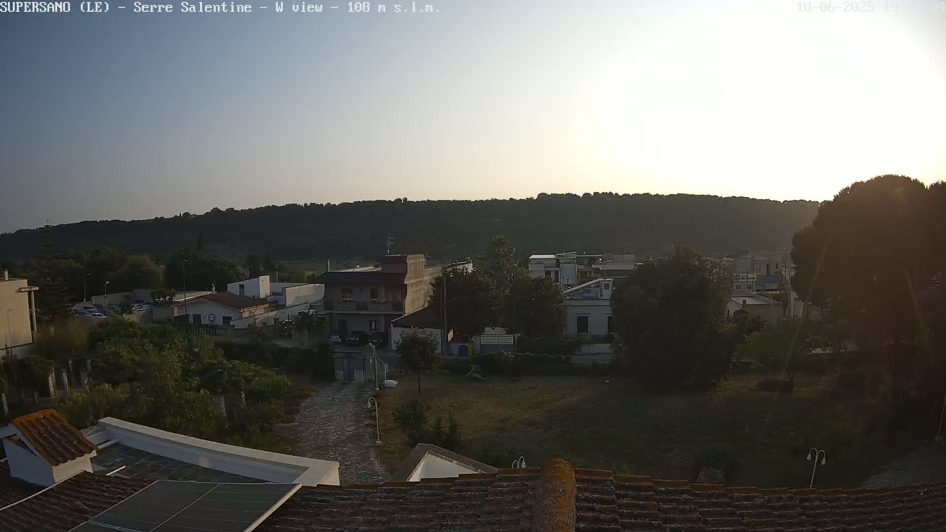 A sunset view over a residential area nestled against a hillside, with clear skies.