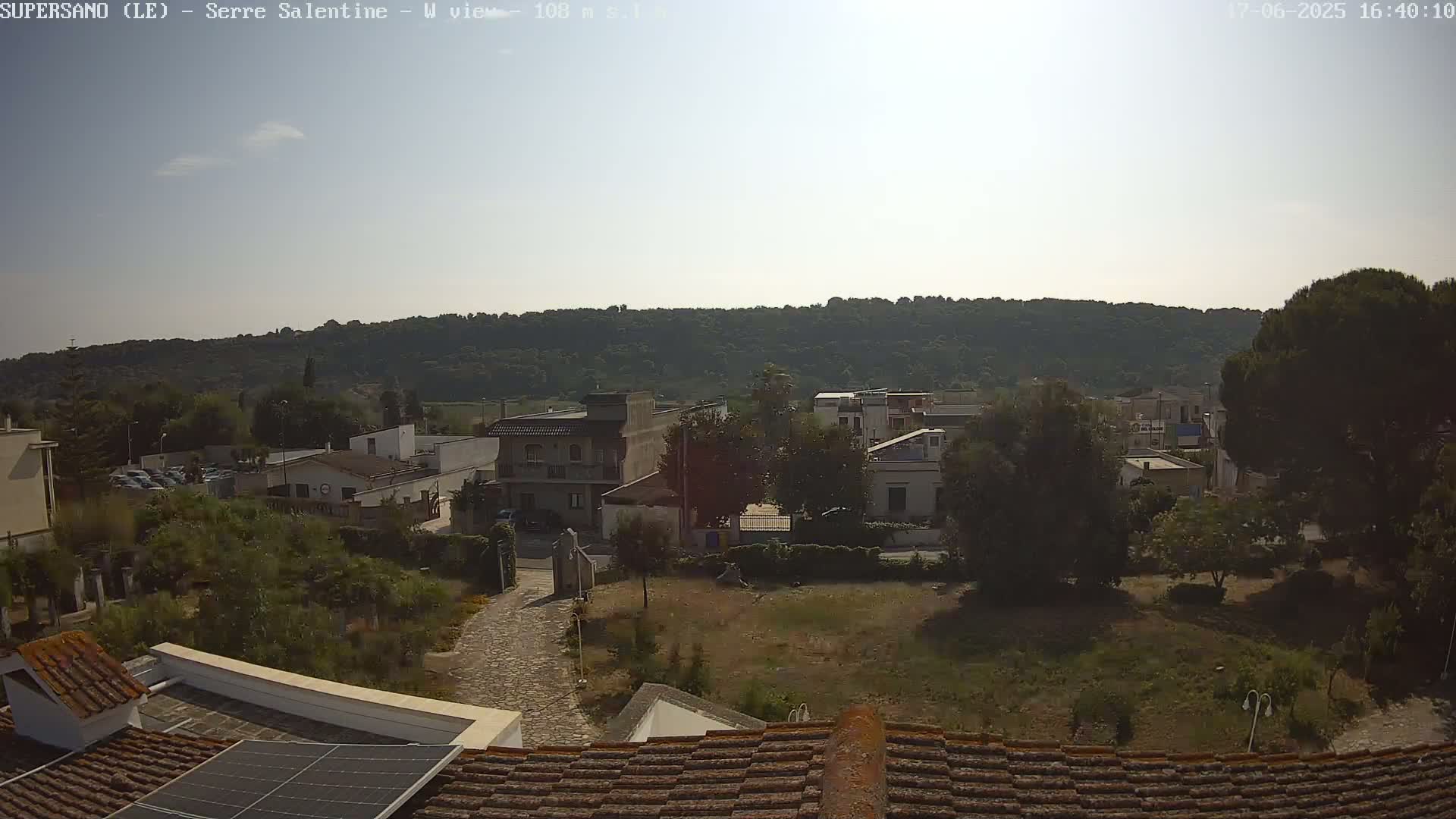 A view of a village nestled at the base of a tree-covered hill on a sunny day.