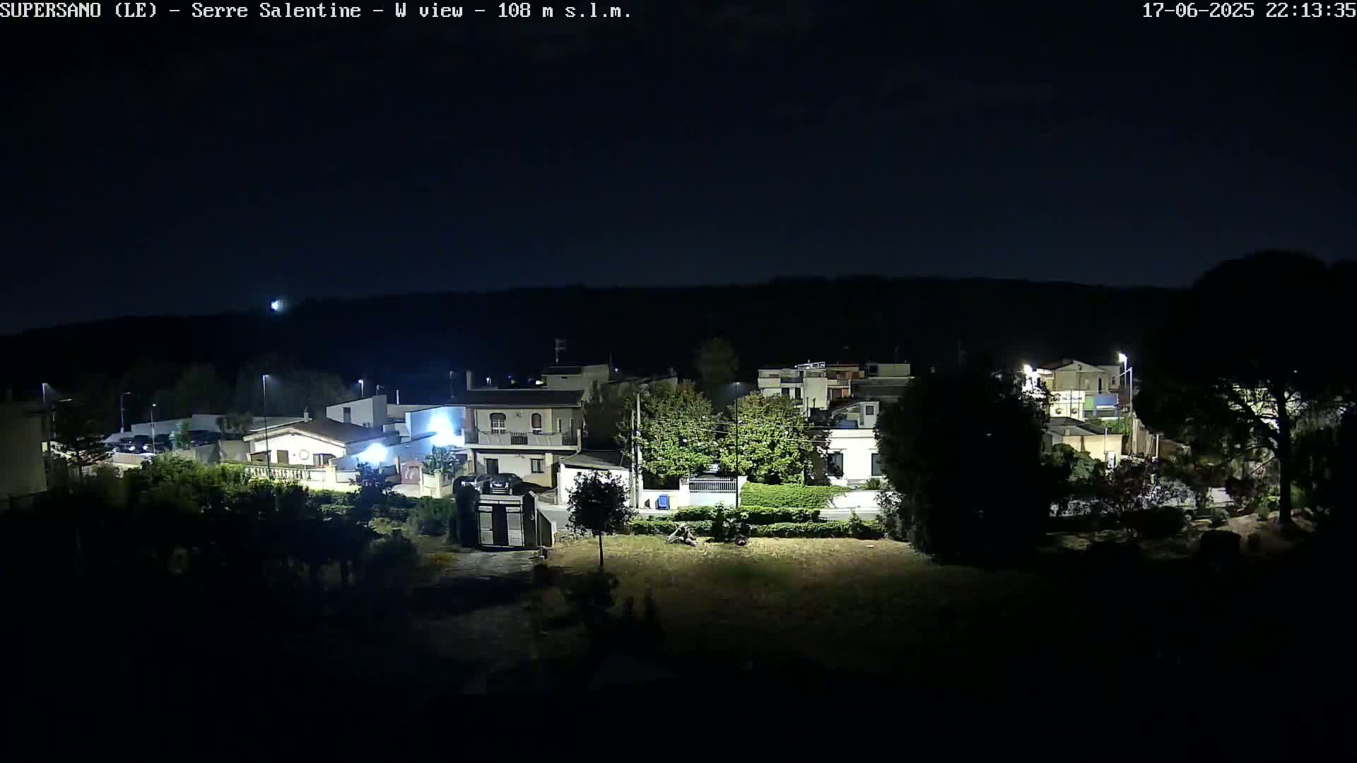 A nighttime, aerial view of a residential area with houses and streetlights illuminated against a dark sky.