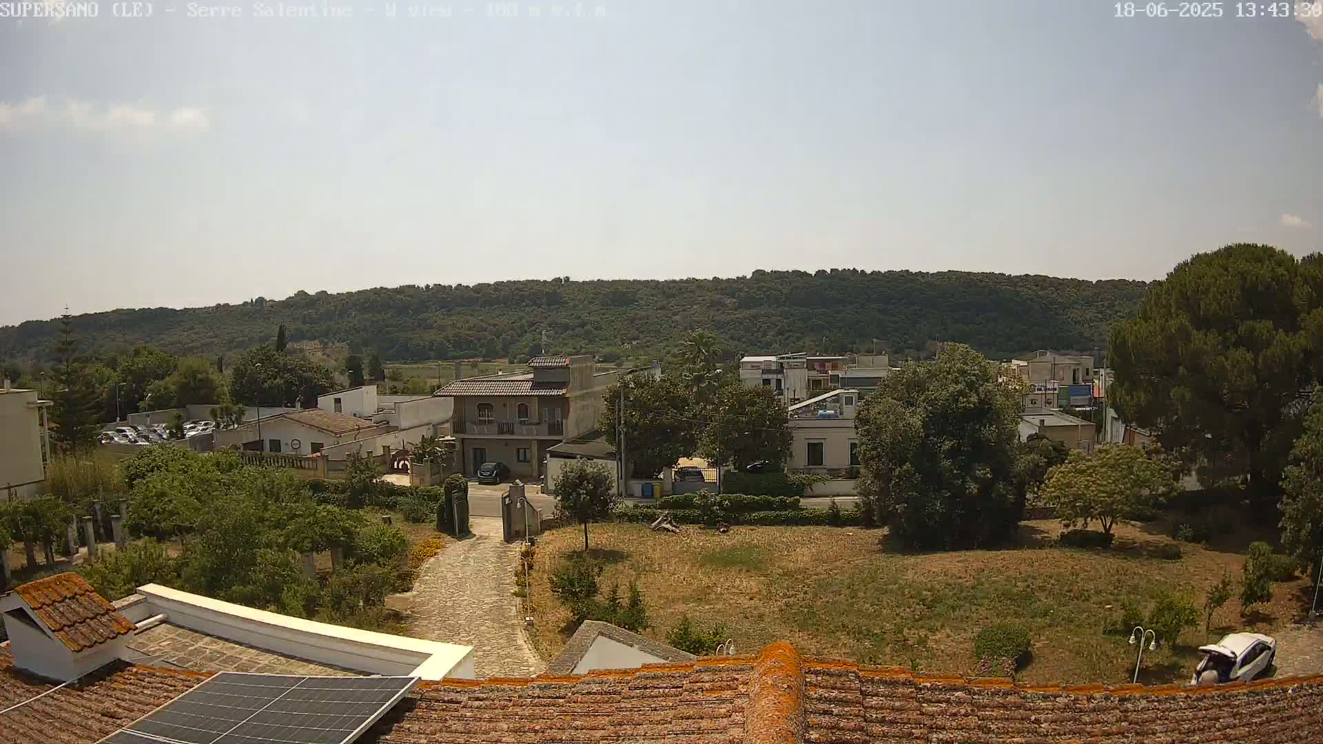 A sunny day overlooking a small town nestled against a verdant hillside, with a paved driveway leading towards several buildings.