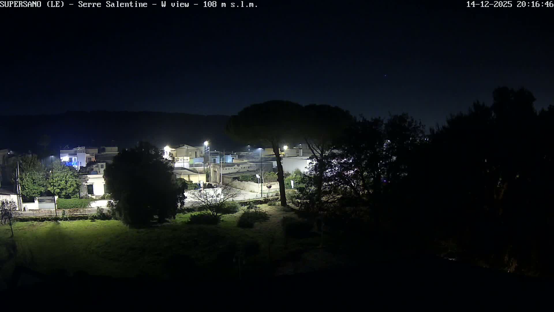 On a clear and sunny day, the scene overlooks a terracotta tiled roof towards a verdant landscape with various trees, a village, and a densely forested hill in the background.
