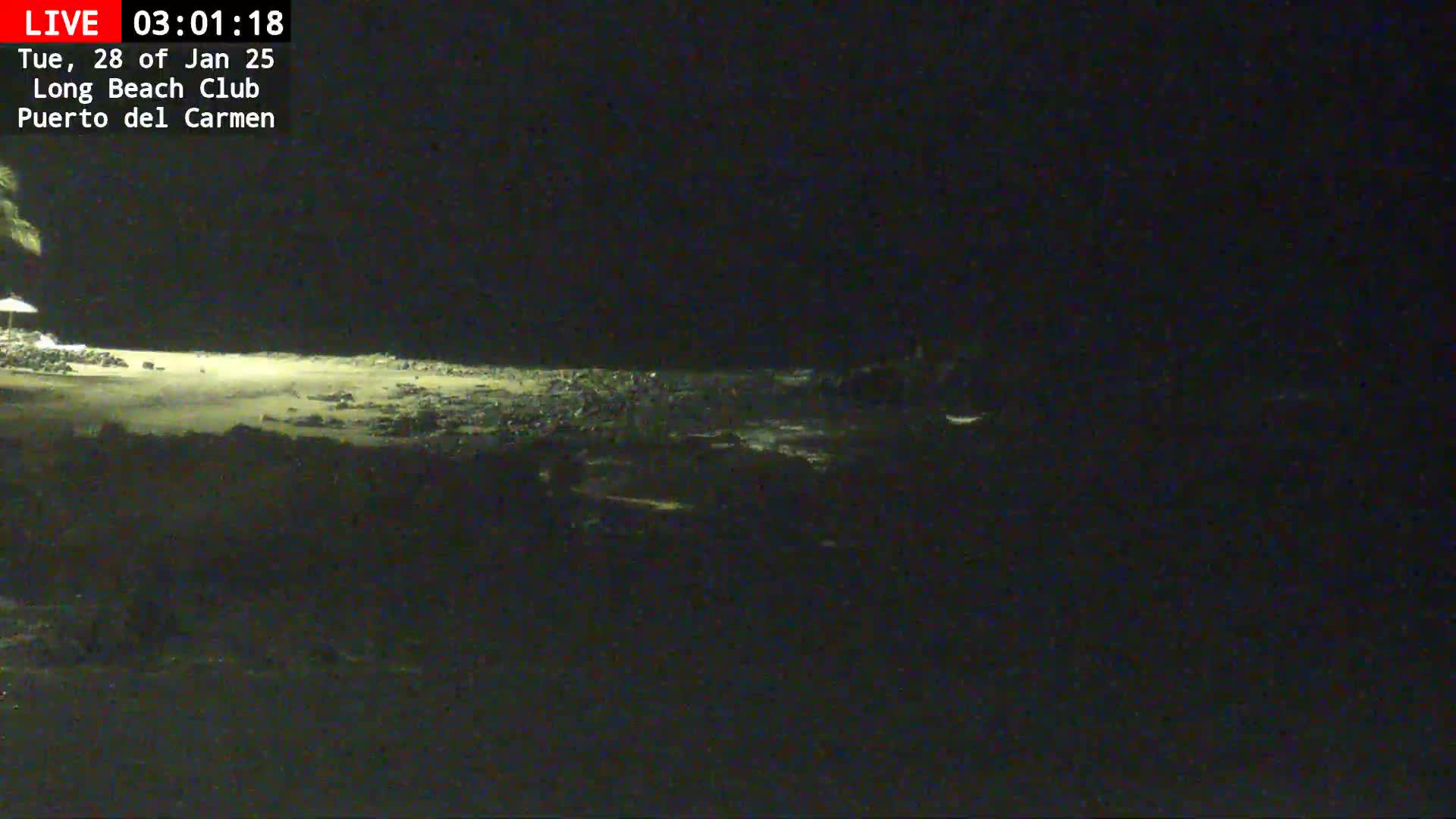 A dark, nighttime view of a beach with a rocky shoreline under a clear sky.