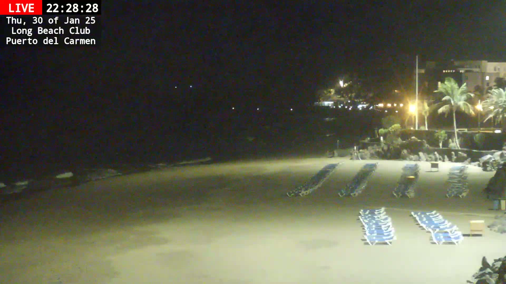 Rows of empty lounge chairs sit on a sandy beach at night under a dark sky.