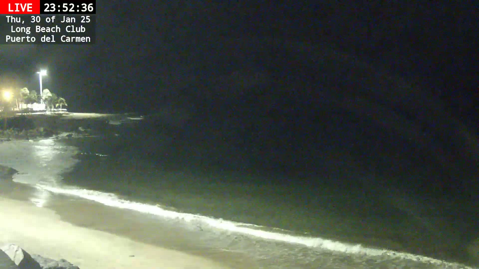 A nighttime beach scene shows gently lapping waves on a sandy shore under a dark sky.