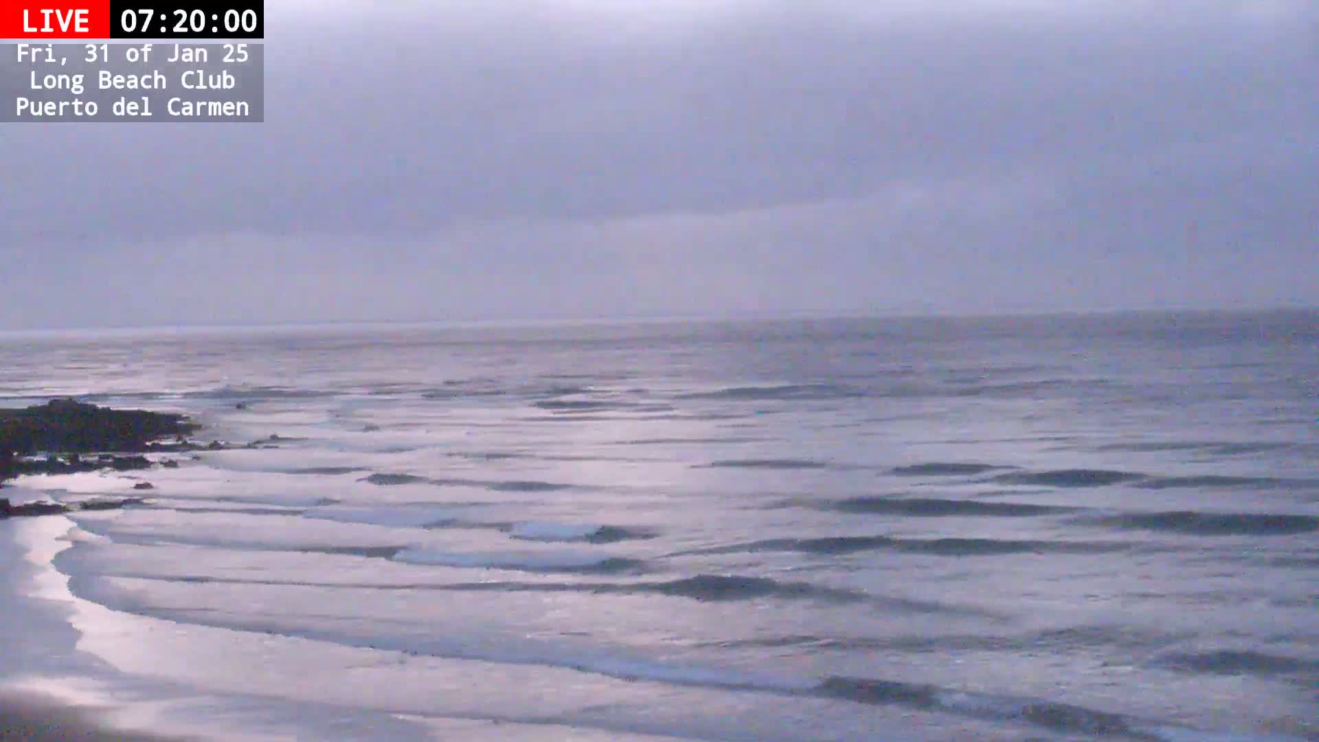 A sandy beach meets a calm ocean under an overcast sky.