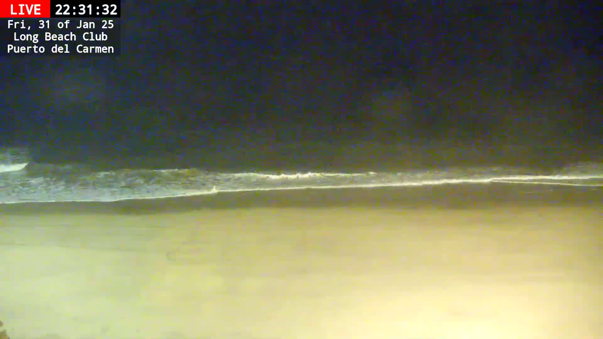 A sandy beach at night is gently lapped by waves under a dark sky.