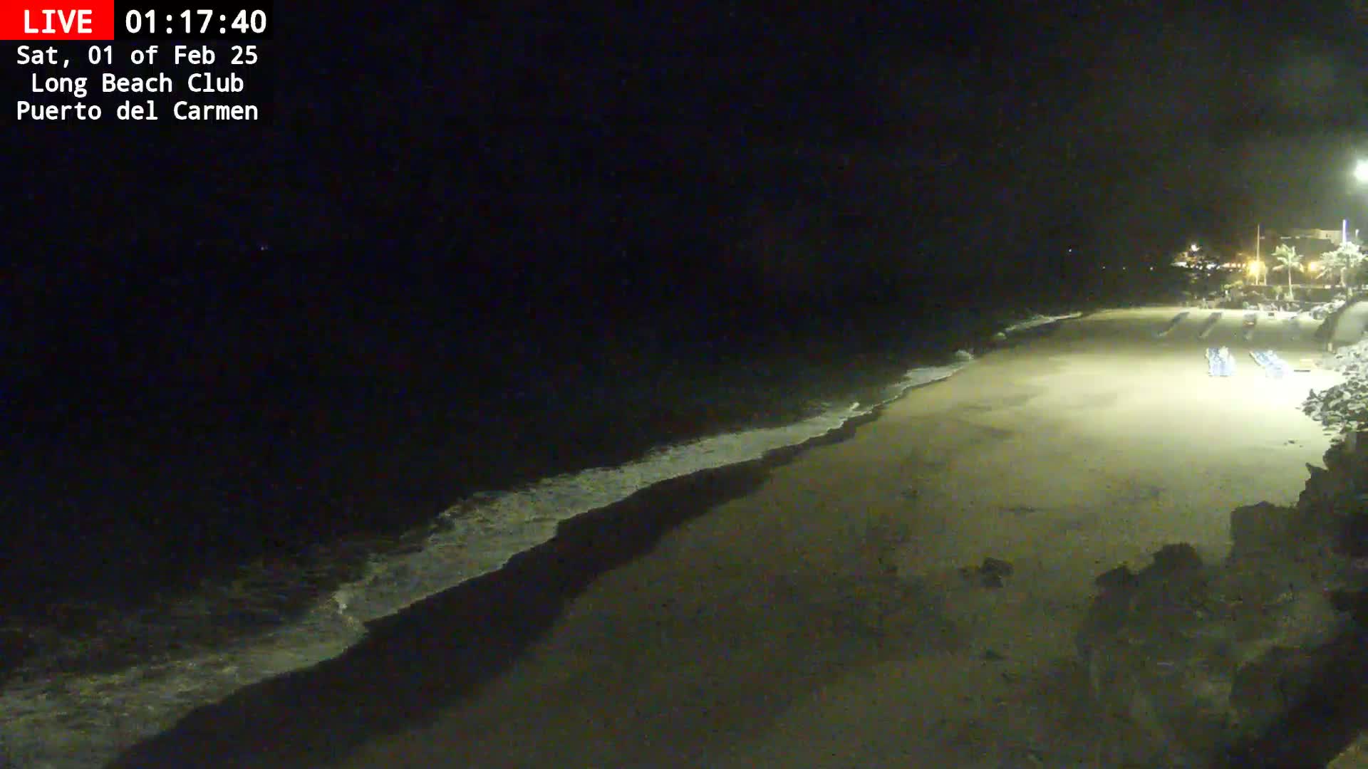A dark, sandy beach at night is gently lapped by small waves under a clear, starless sky.
