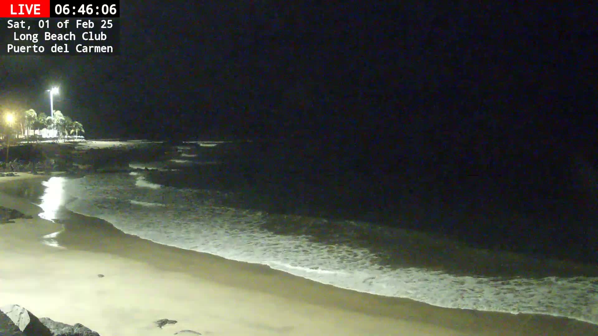 A sandy beach at night with gentle waves lapping the shore under a dark sky.