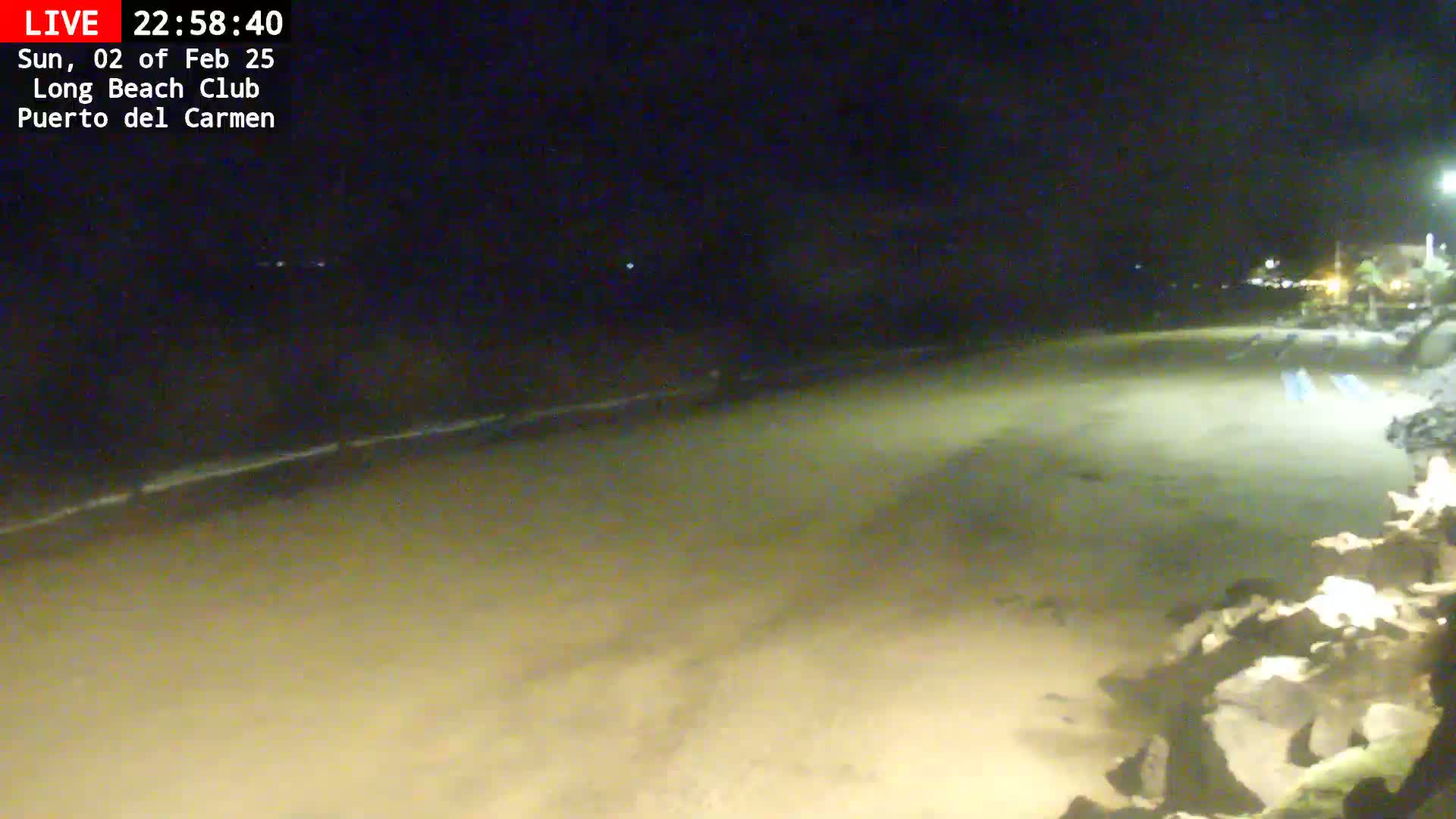 A dark, sandy beach is visible at night, with a calm ocean in the background.