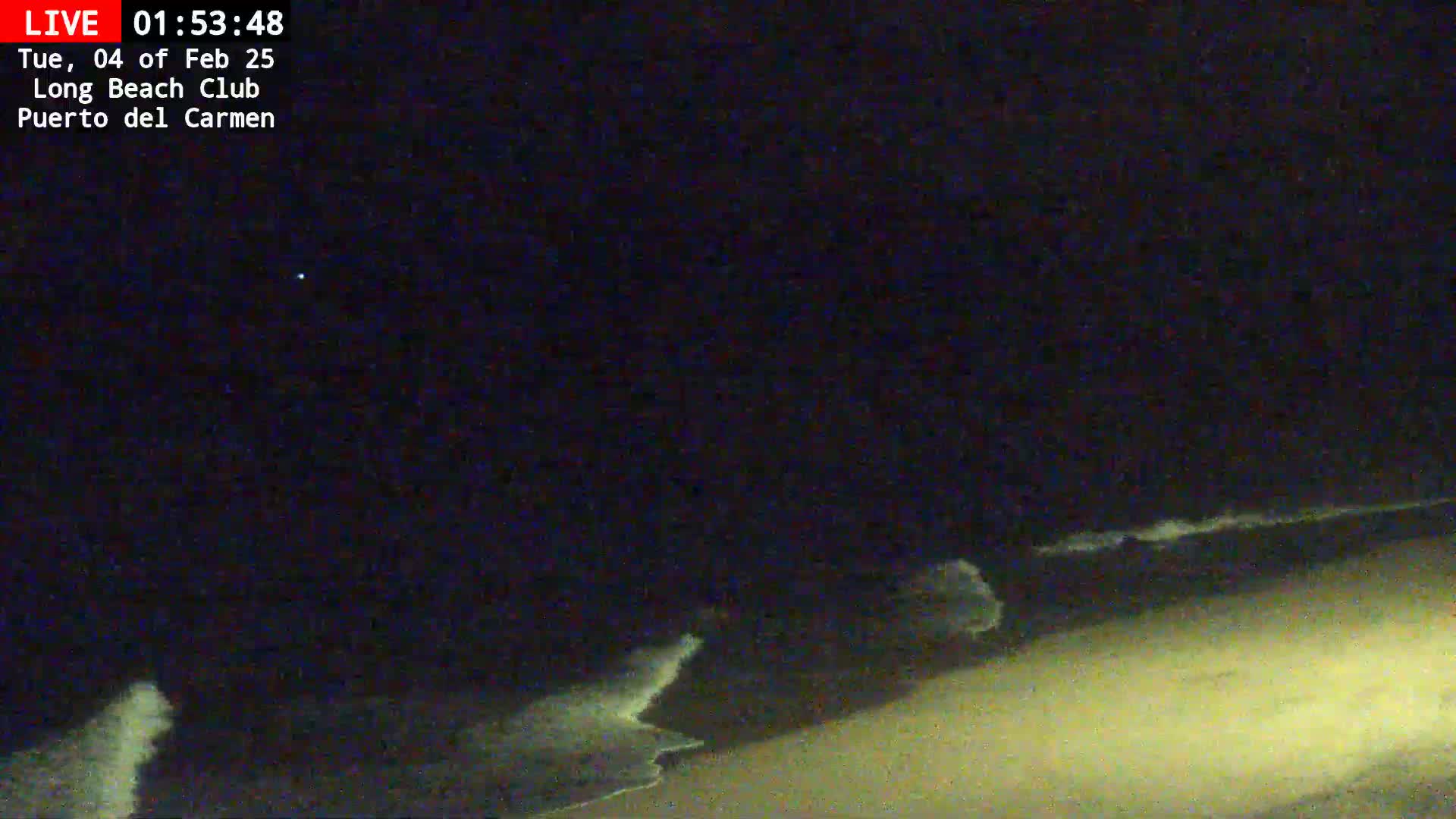 A nighttime beach scene shows dark sand and gently lapping waves under a clear, dark sky.